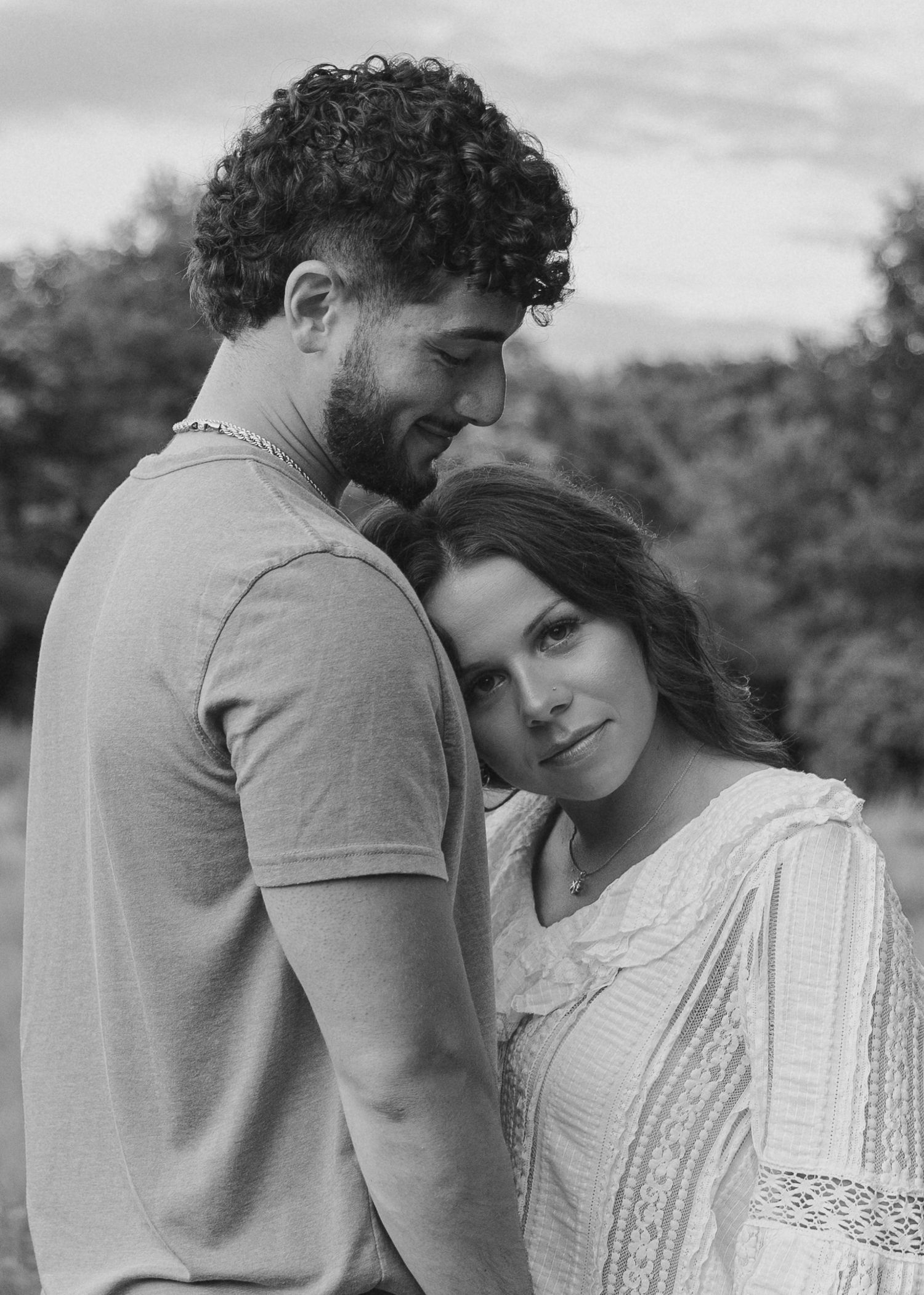 Black and white portrait of a romantic couple embracing outdoors, woman resting head on man's chest.