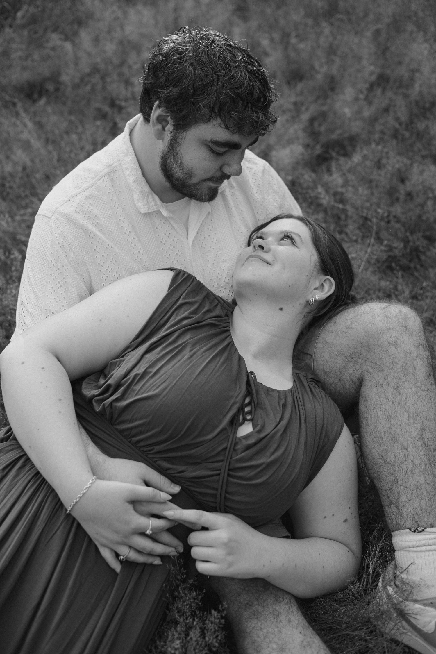 Black and white photo of a couple sharing a romantic moment outdoors, woman in flowing dress leaning back against man.