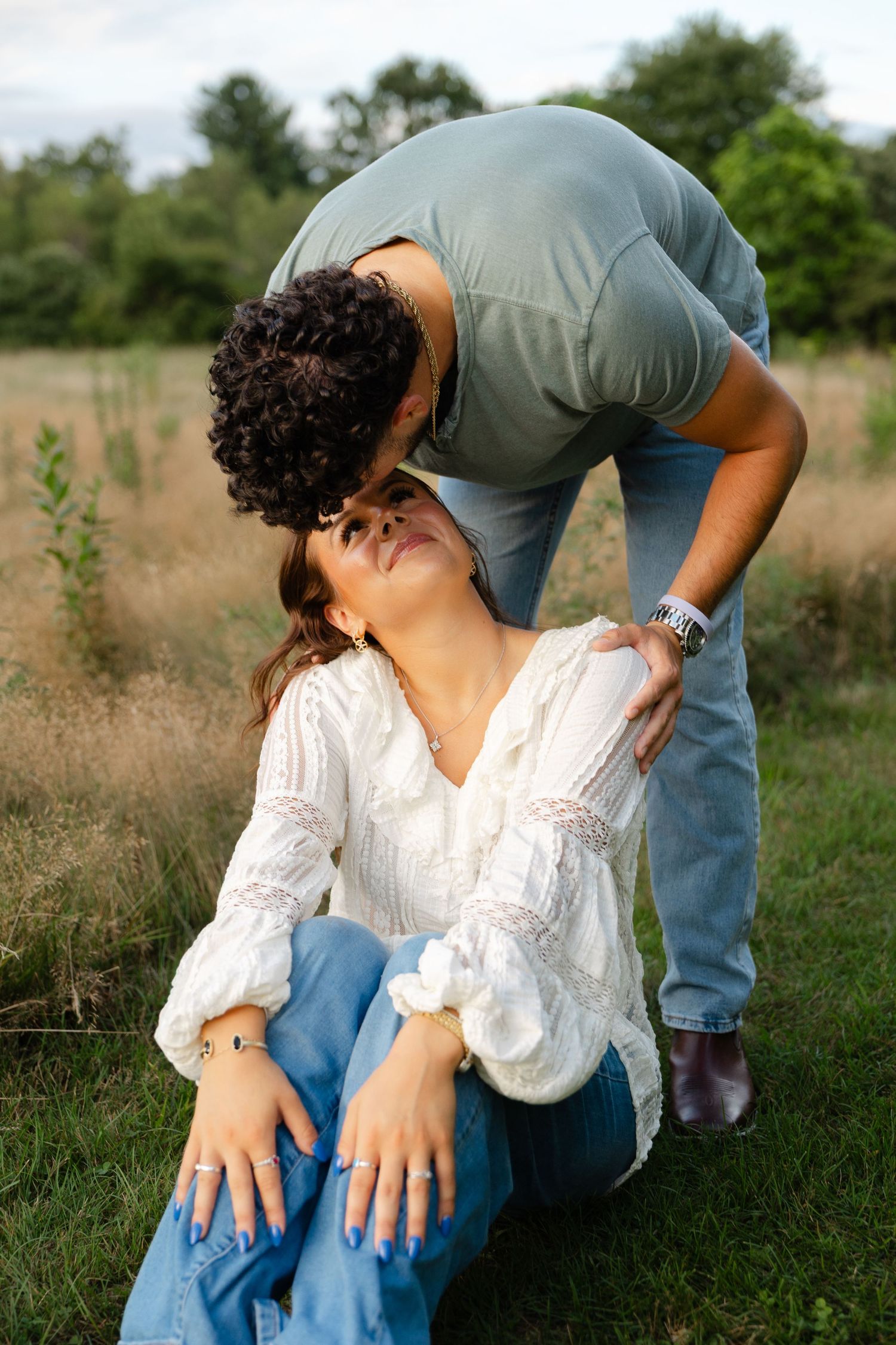 A man tenderly kisses a woman on the forehead as she sits in a grassy field during a romantic outdoor couples session.