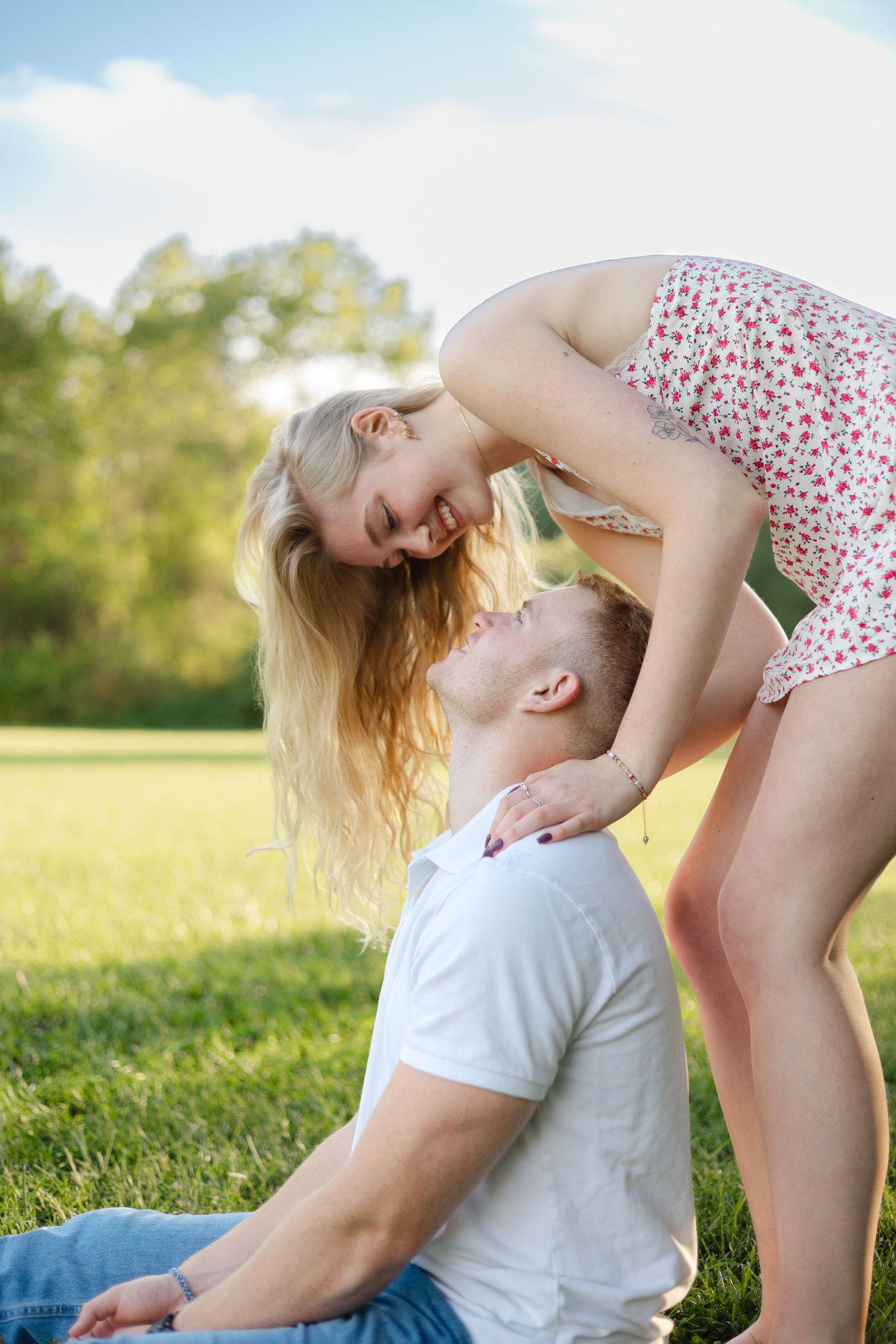A happy young couple sharing a romantic moment on green grass in a sunny park, woman leaning over smiling man.