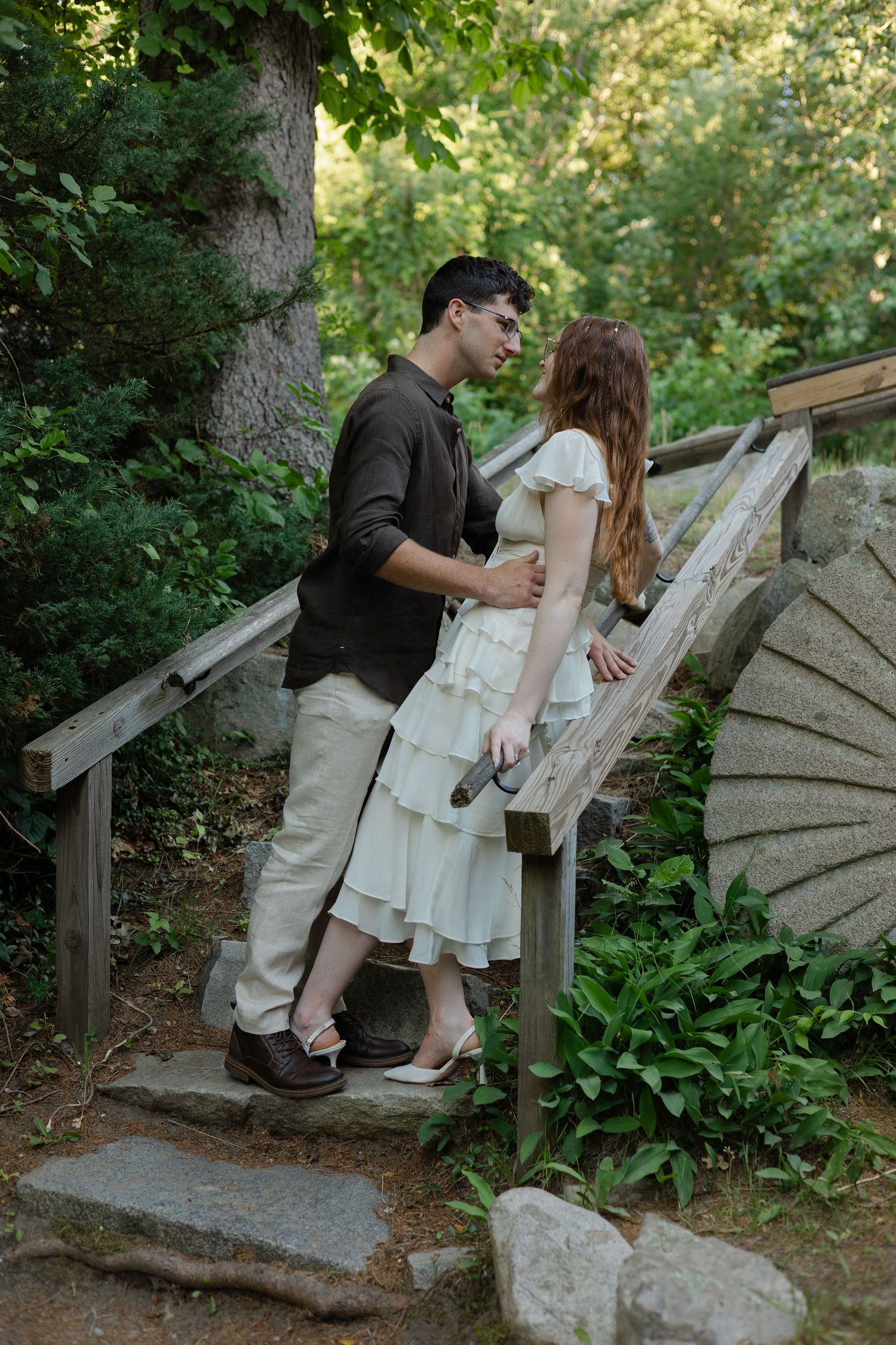 Couple sharing a romantic moment on wooden garden steps surrounded by lush green foliage.