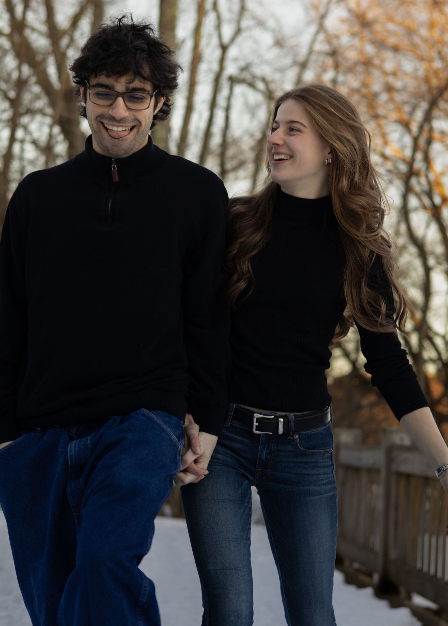Happy young couple holding hands and laughing while walking together on a snowy path in winter.