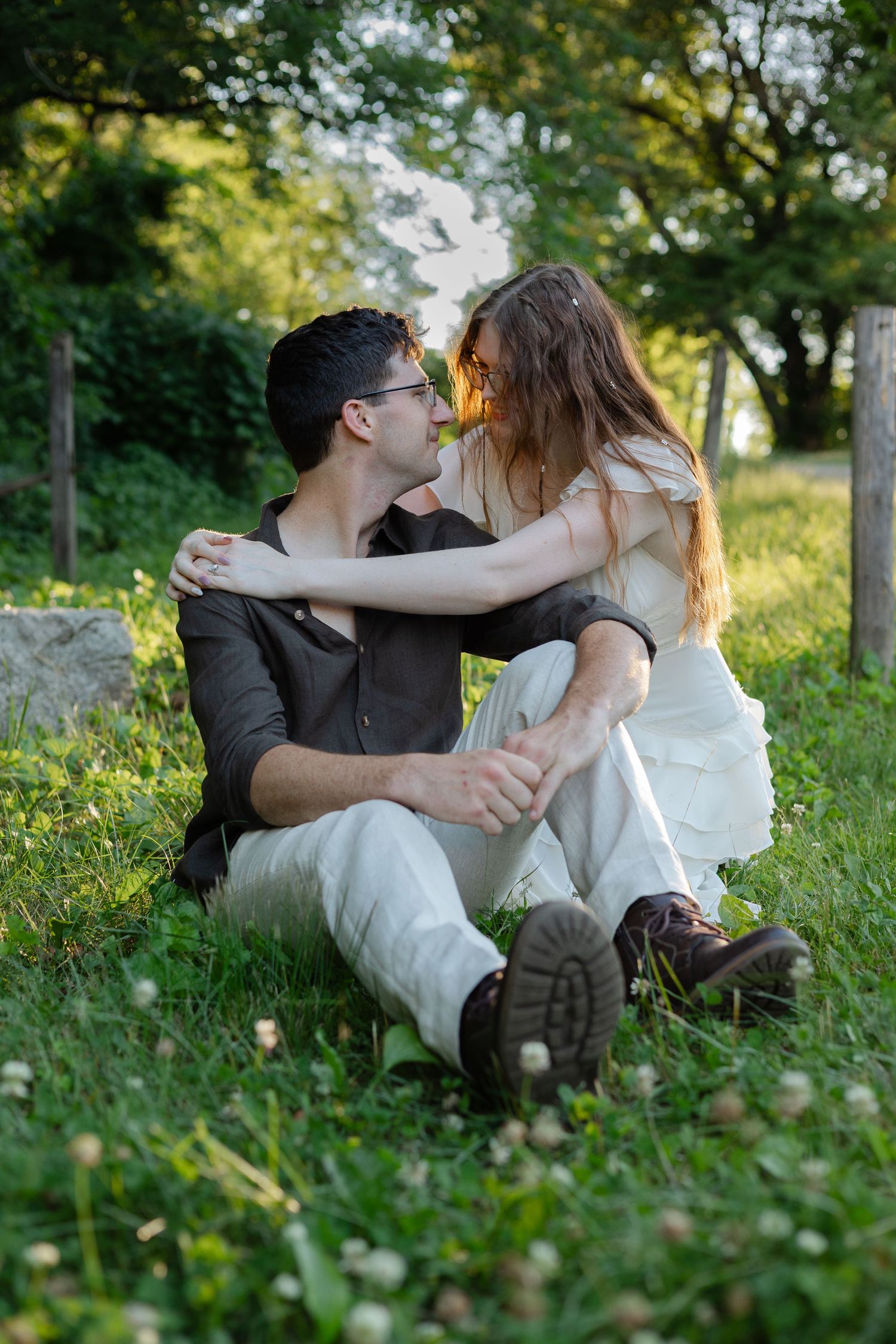 Couple sitting on grass in a park, embracing and gazing at each other romantically in golden sunlight.