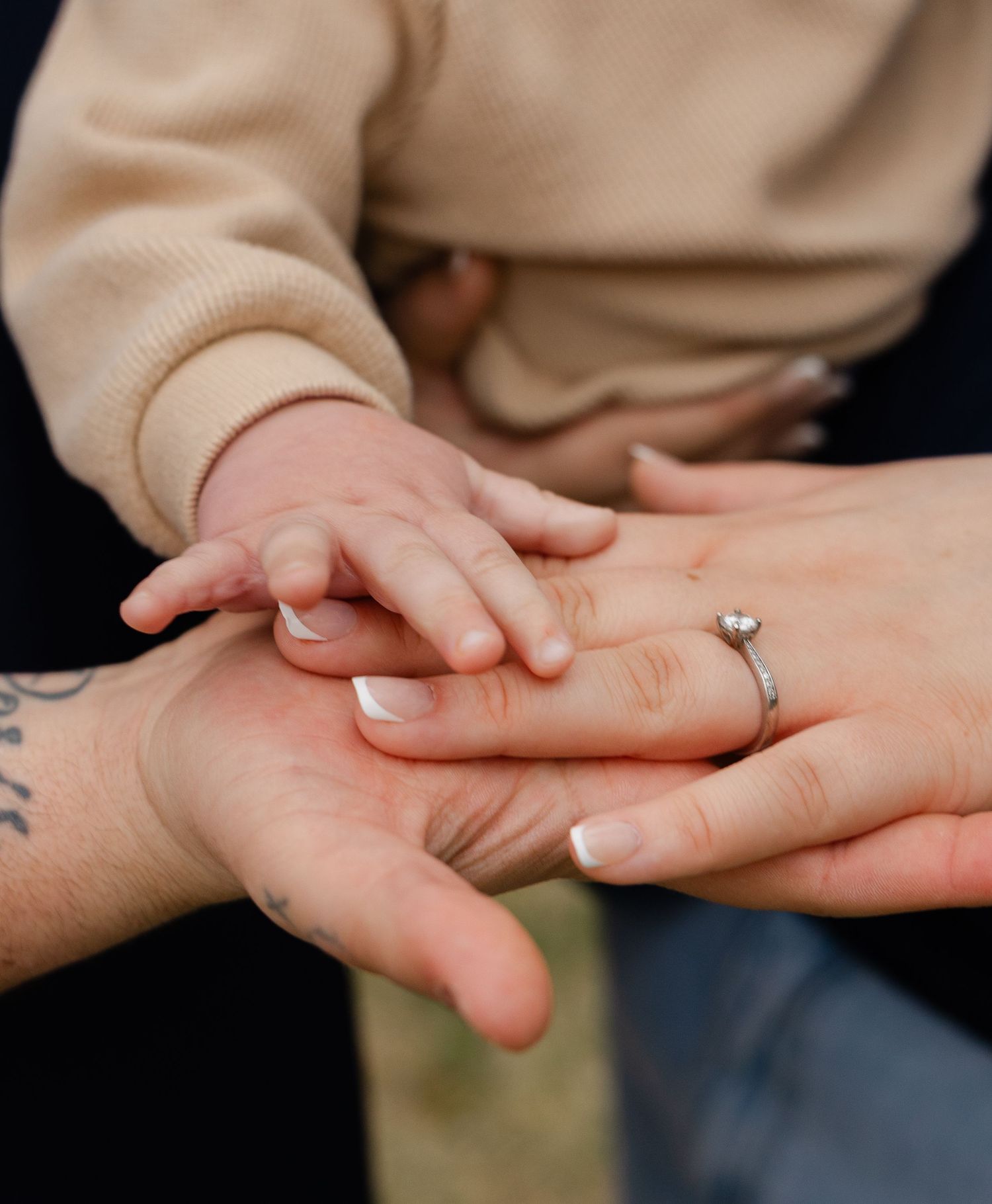 Close-up of baby hand resting on parents hands, mother wearing diamond engagement ring.
