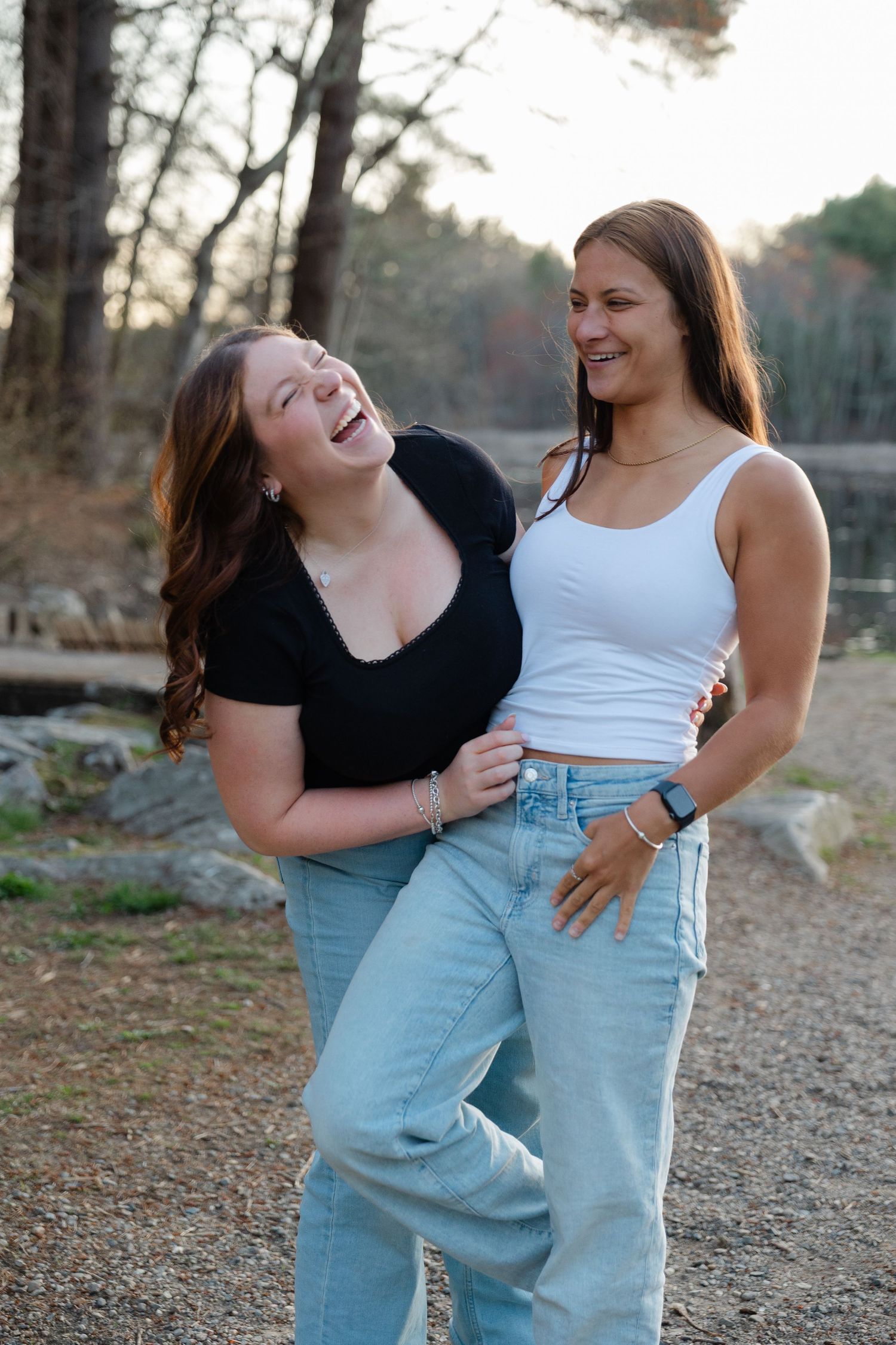 Two young women laughing together outdoors near a scenic lake setting.