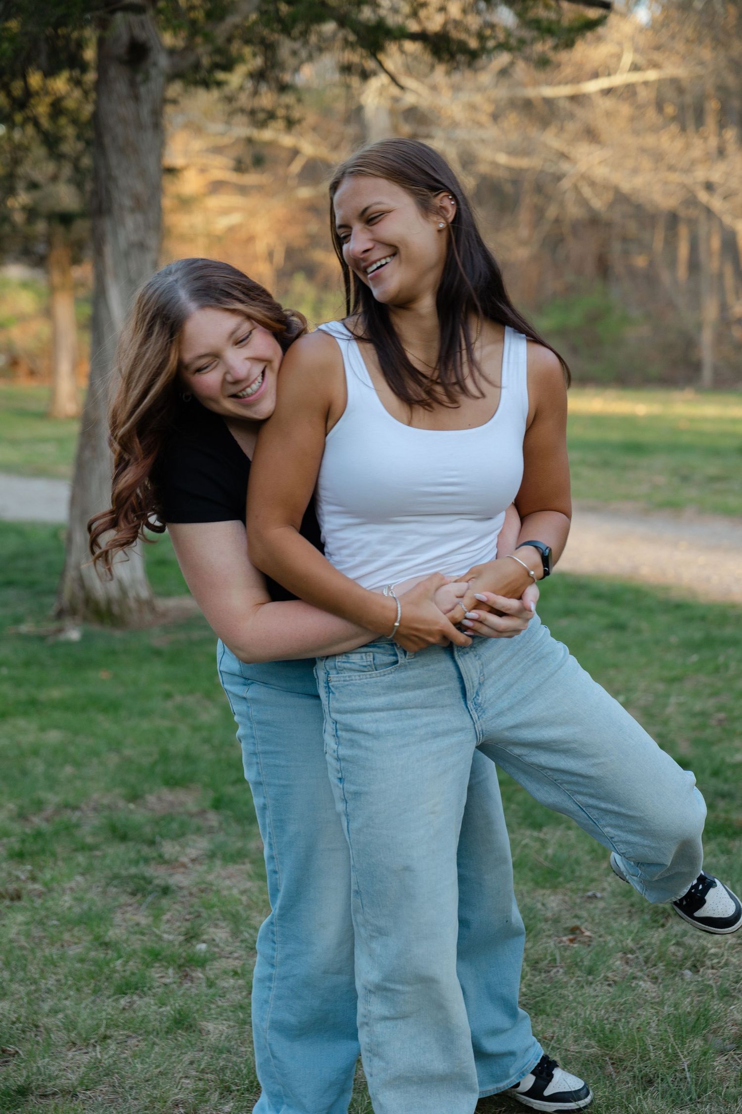 Two laughing young women playfully embracing in a sunny green park.