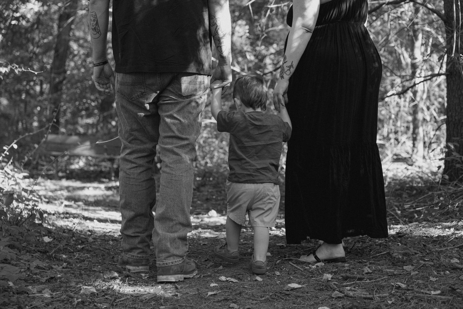 Black and white photo of a family with a toddler holding parents hands in a forest setting.