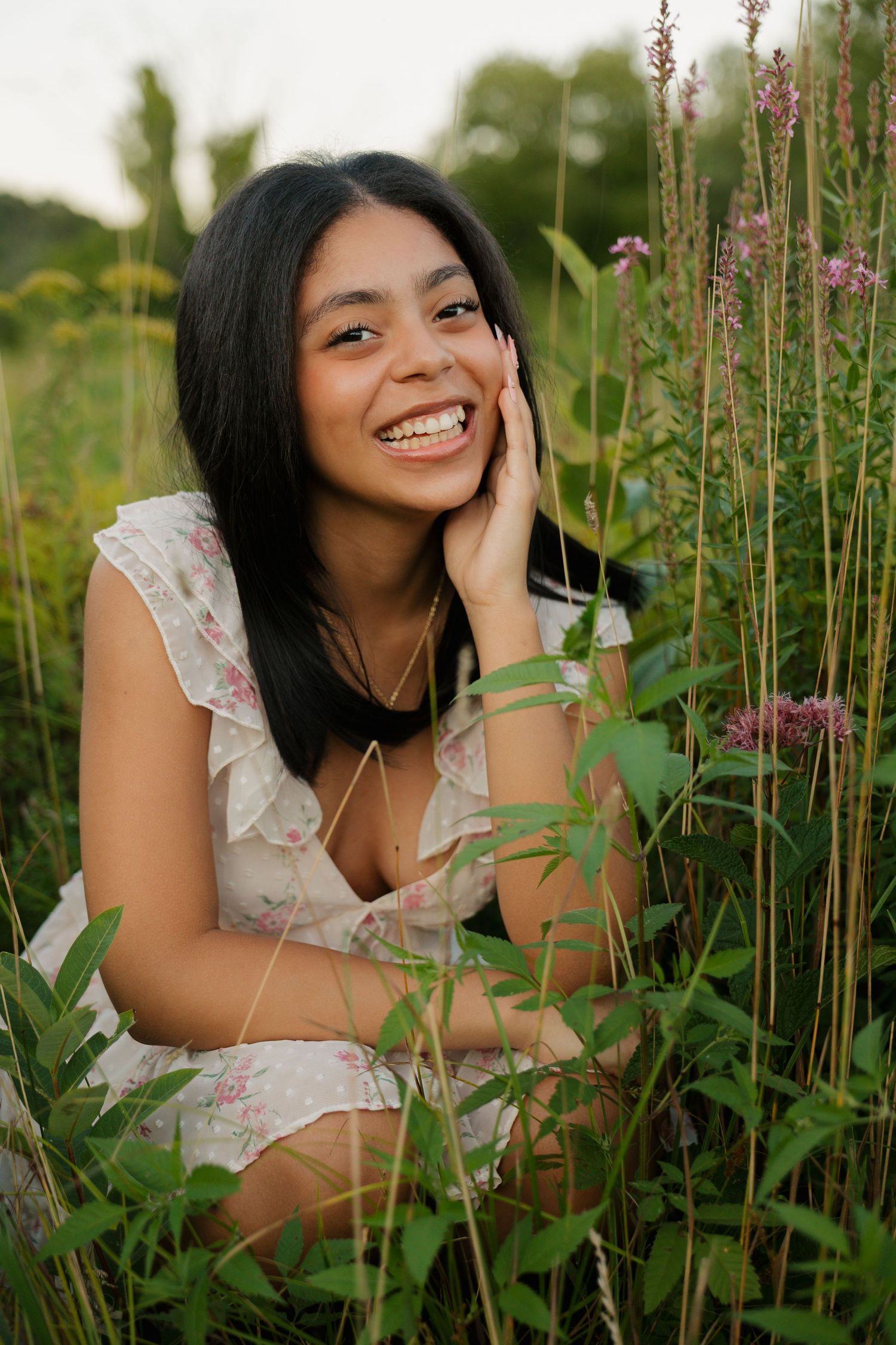 Young woman in floral dress smiling joyfully among wildflowers in a lush green field.