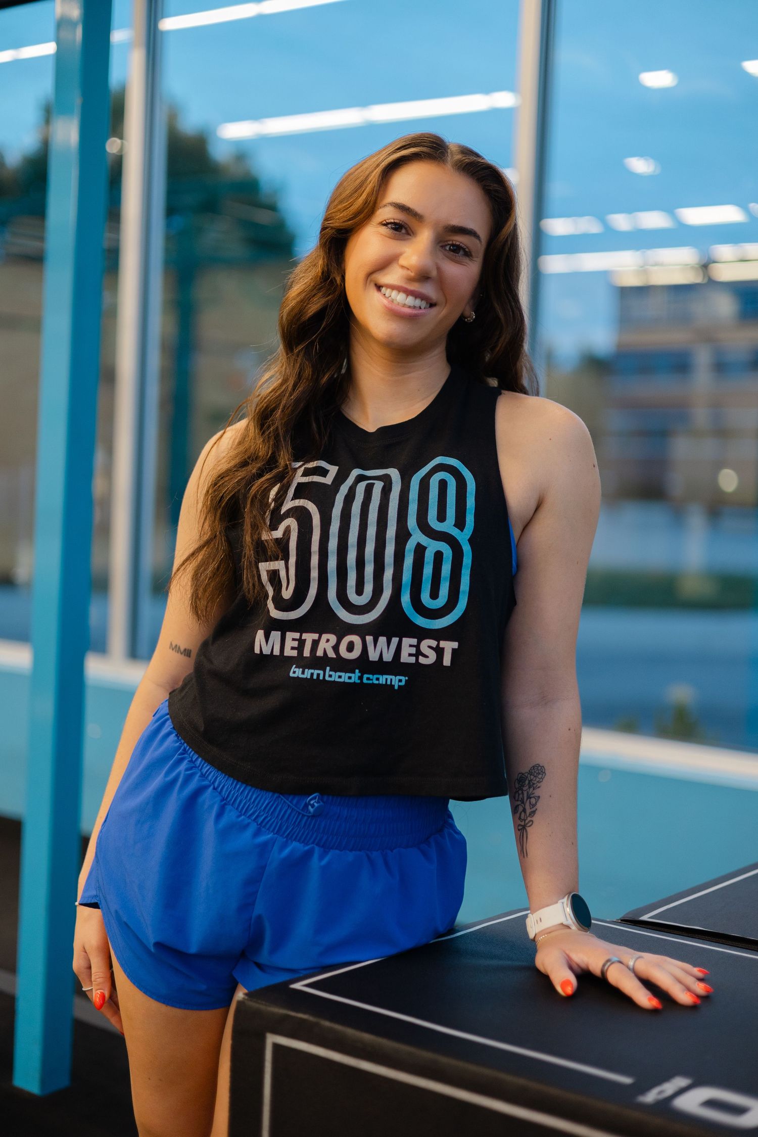 Smiling woman in 508 Metrowest black tank top and blue shorts posing at a fitness camp.