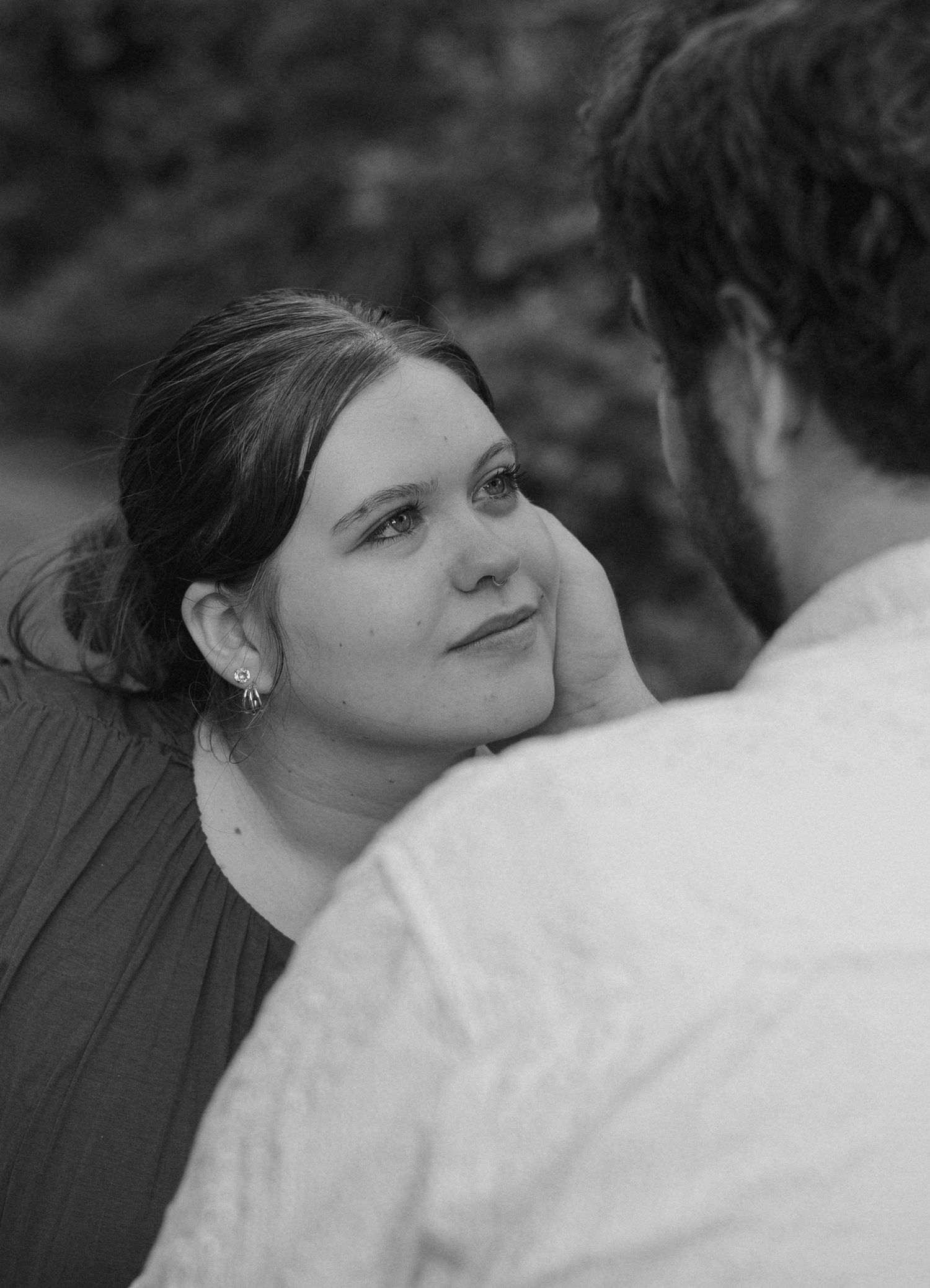 Black and white romantic couple portrait, woman gazing lovingly at man while he tenderly cups her face outdoors.