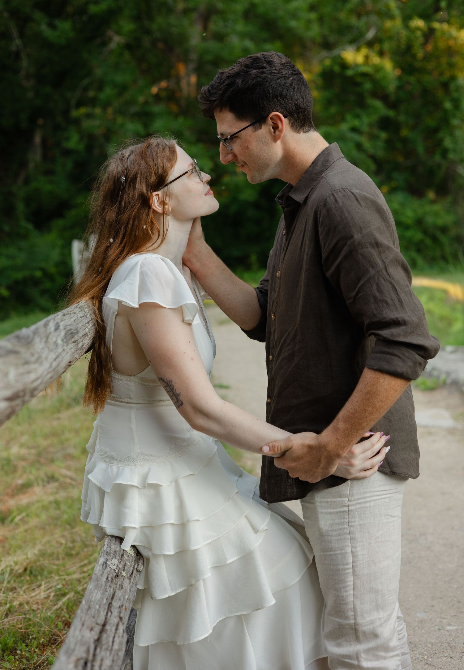 A couple in a tender moment outdoors, woman in white ruffled dress, man in dark shirt gently touching her face.