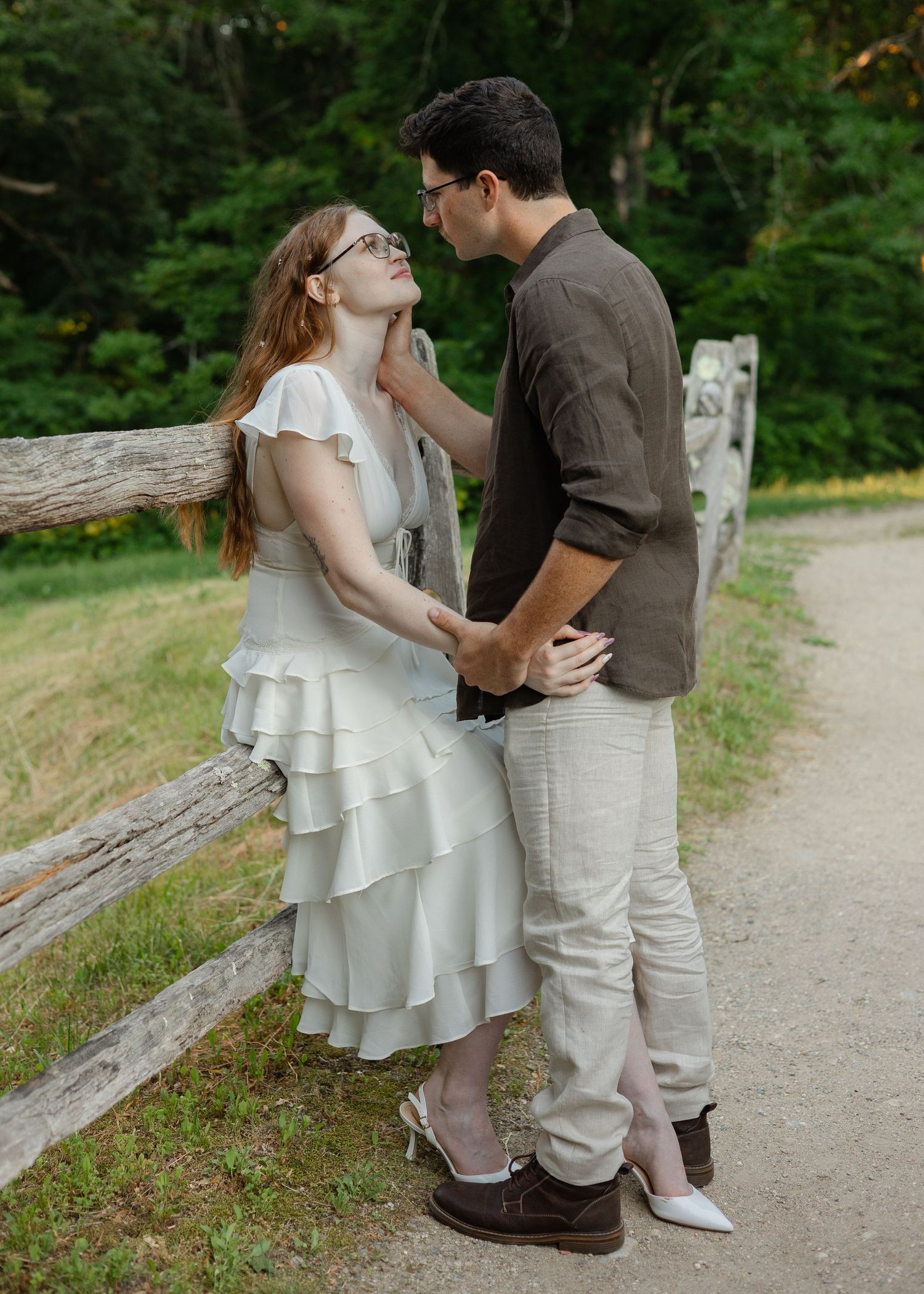 A couple shares a romantic moment on a garden path, the woman in a white ruffled dress gazing up at her partner.