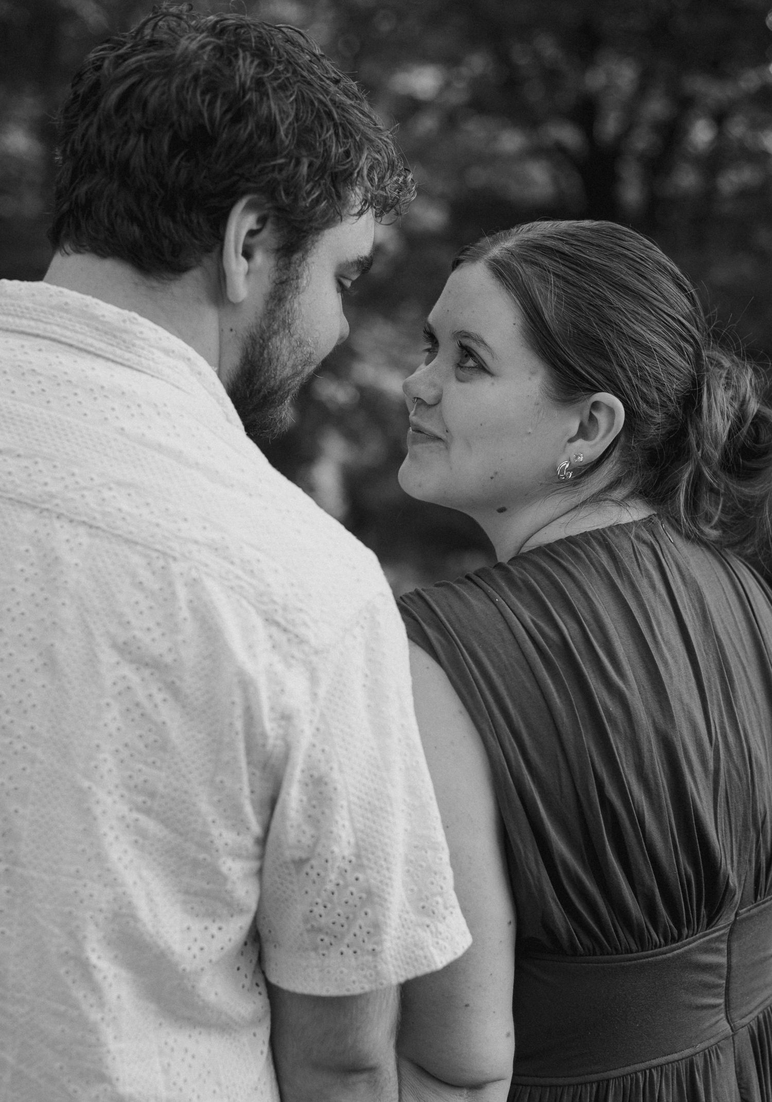 Black and white photo of a couple sharing an intimate moment outdoors, woman smiling at man in white shirt.