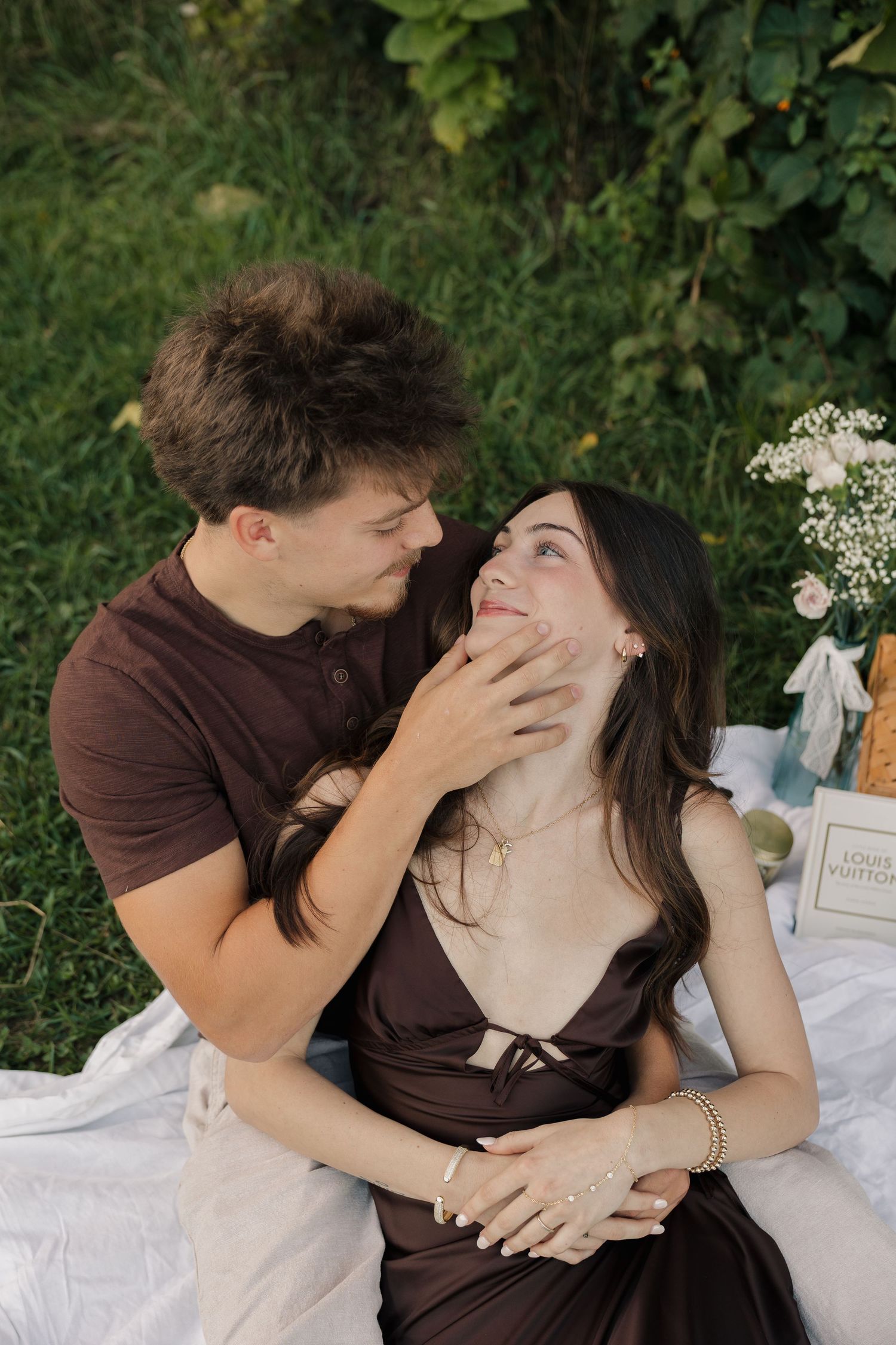 Couple sharing a romantic moment on a picnic blanket in a lush green garden, man tenderly holding womans face.