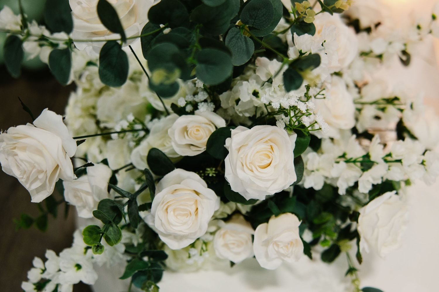Close-up of white roses and eucalyptus floral arrangement with delicate white filler flowers.