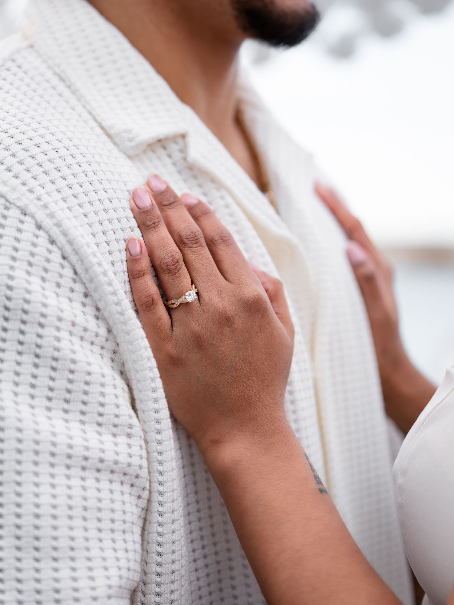 Close-up of a woman's hand with a gold ring resting on a man's white waffle-knit shirt.