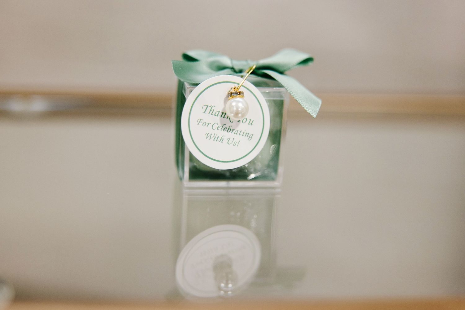 Clear gift box baptism favor with sage green ribbon bow and personalized thank you tag.