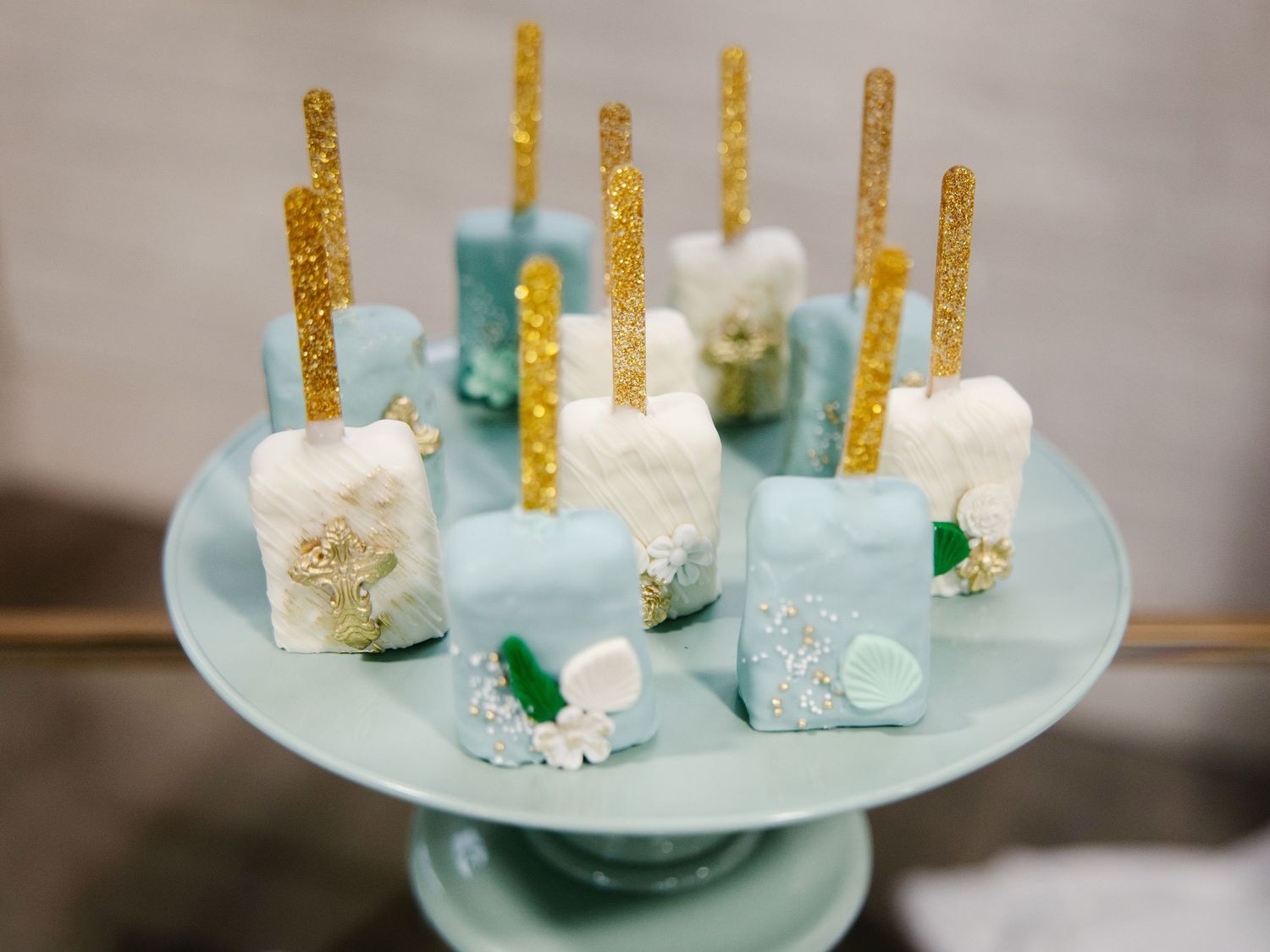 Decorative blue and white chocolate cake pops with gold glitter sticks on display stand.