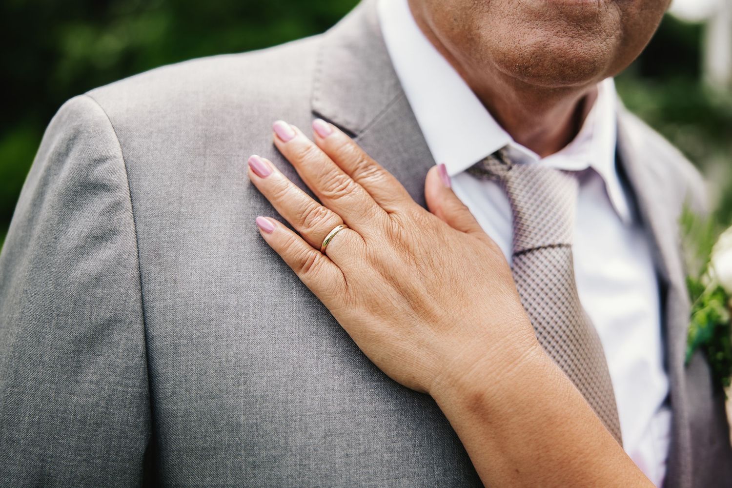 Bride's hand with wedding ring resting on groom's gray suit jacket during wedding ceremony.