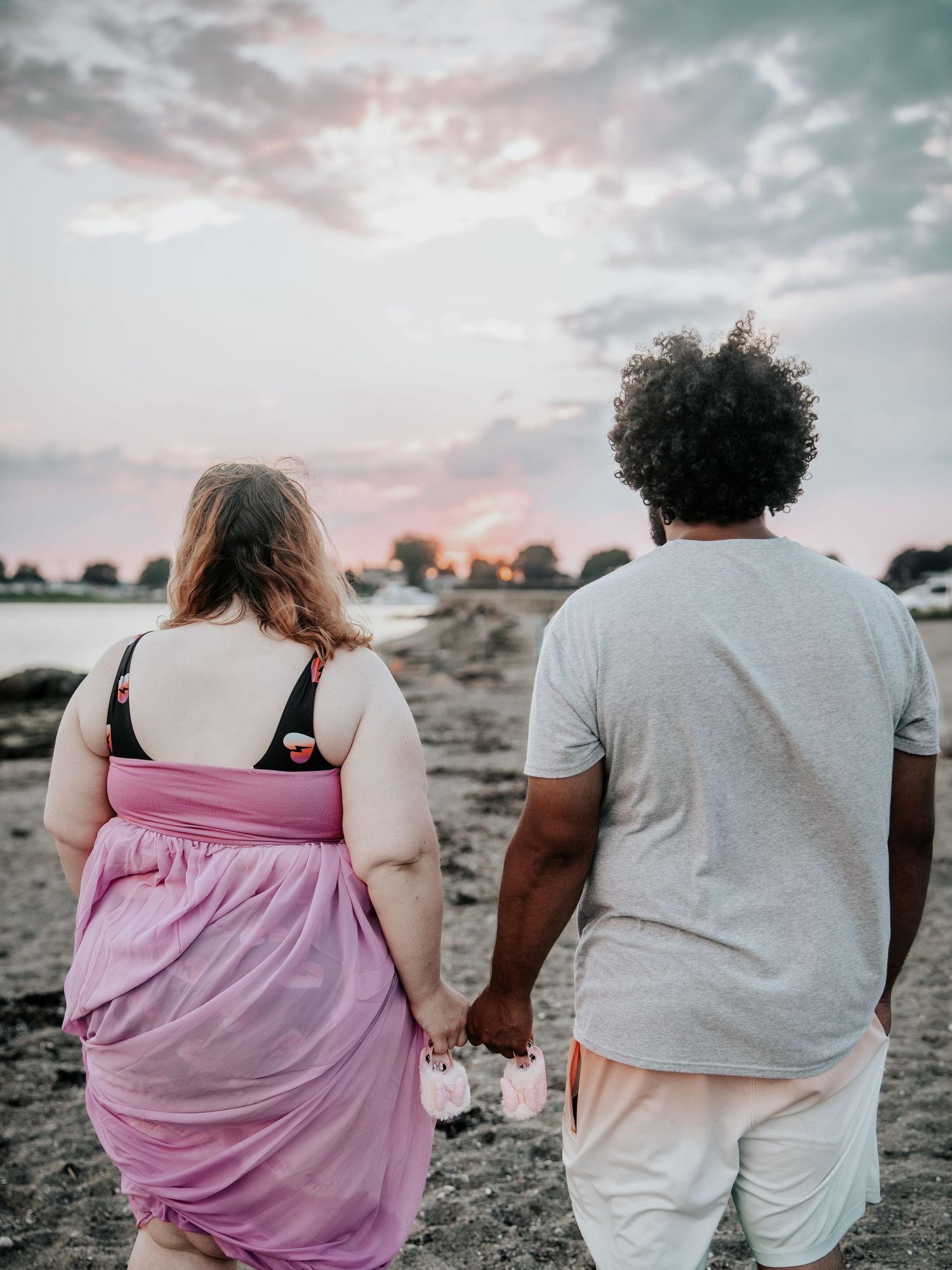 Couple holding hands on a beach at sunset, viewed from behind, enjoying a romantic evening by the water.