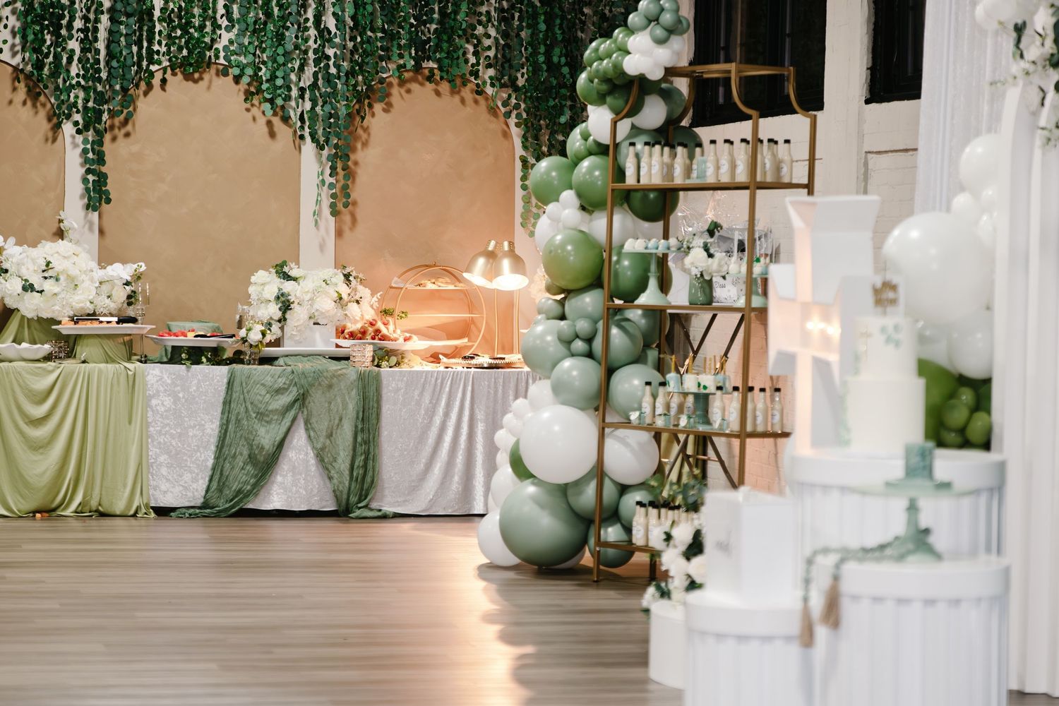Elegant First Communion party venue with green balloon arch, floral centerpieces, and dessert table.