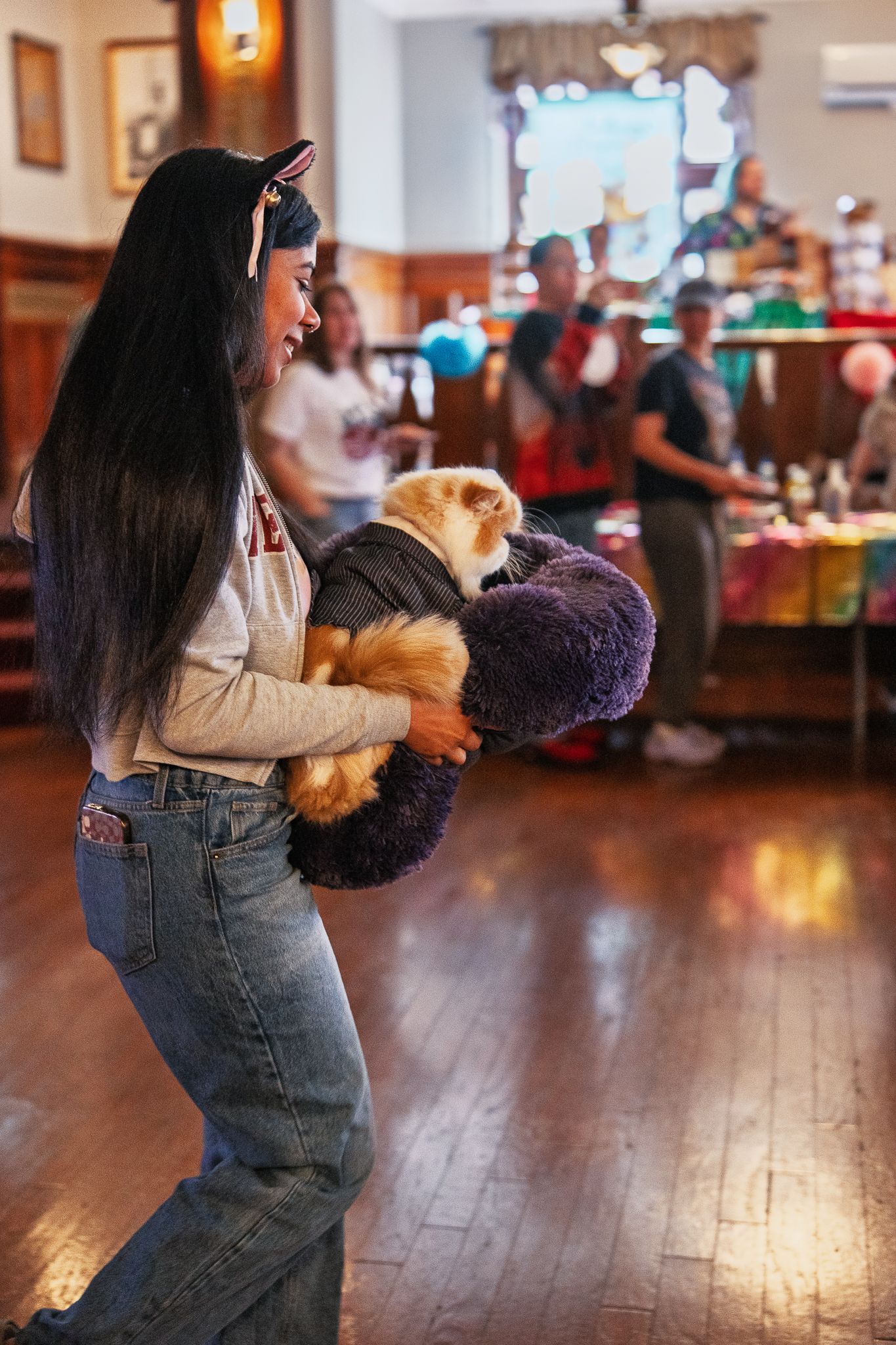 Young woman carrying a fluffy Persian cat dressed in costume at a colorful birthday party celebration.