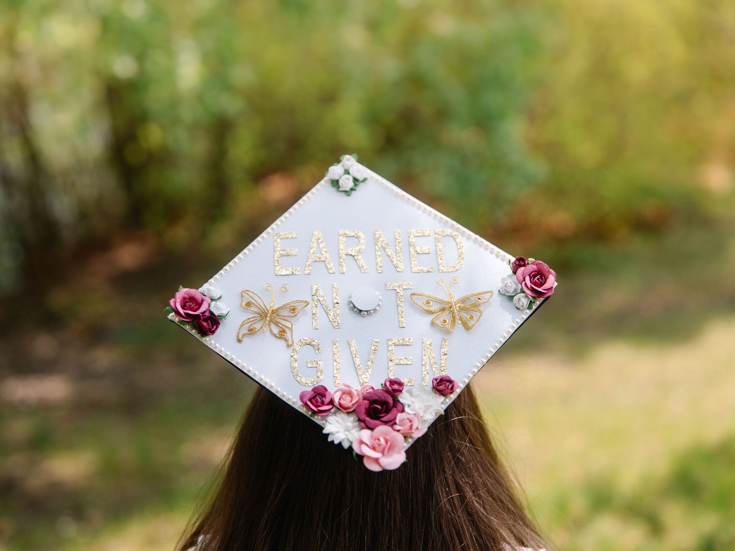 Decorated graduation cap with floral design and gold butterfly accents reading Earned Not Given.
