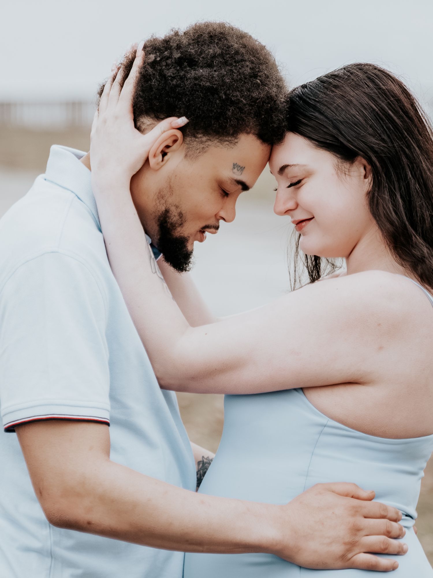A romantic couple tenderly touching foreheads outdoors, the woman smiling softly while embracing her partner in a loving pose.