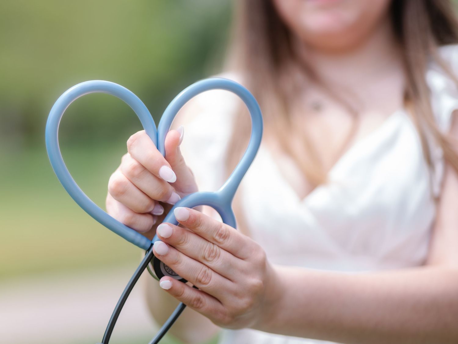Hands forming a heart shape with blue stethoscope tubing, symbolizing healthcare and compassion.