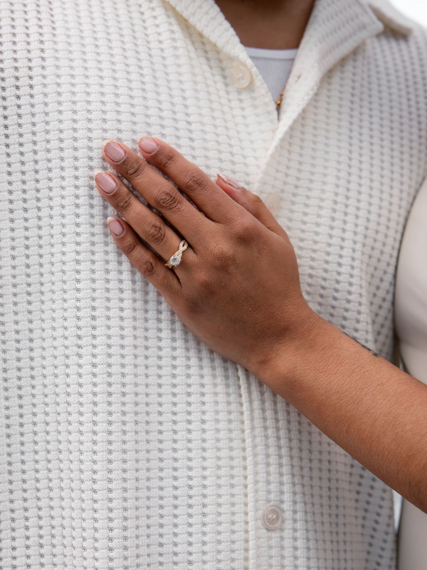Close-up of engagement ring on hand resting on white textured jacket.