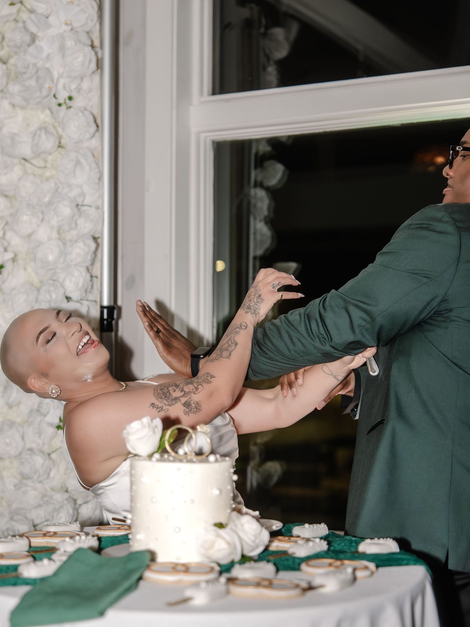 Bride and groom sharing a playful cake cutting moment at their wedding reception with white floral backdrop.