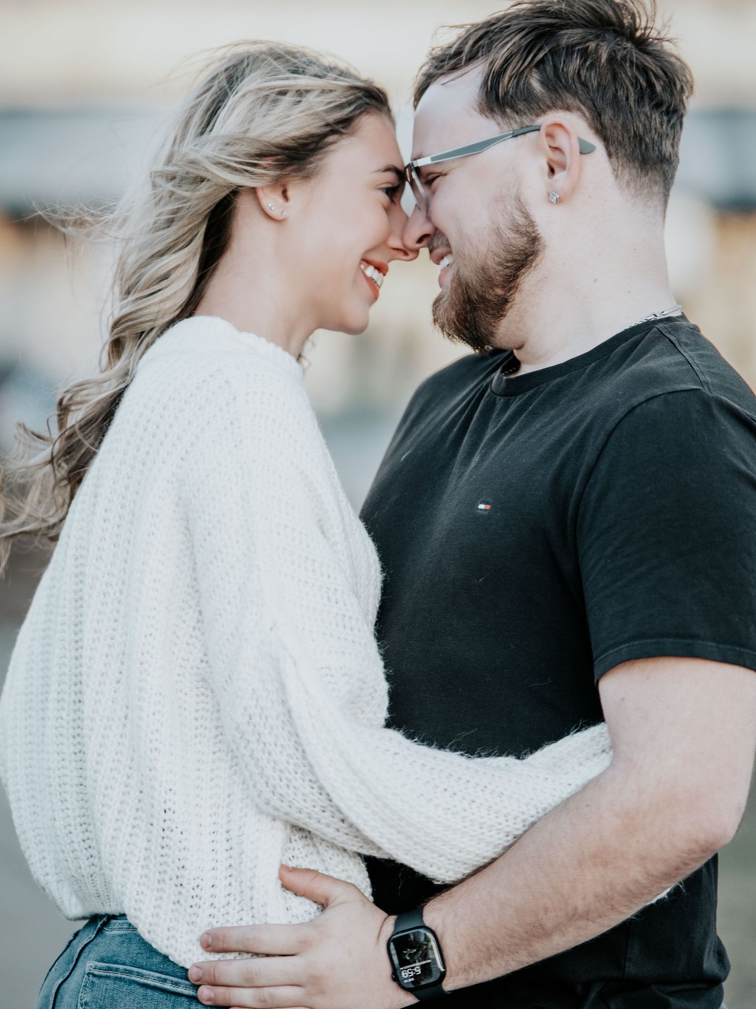 Romantic couple touching foreheads and embracing outdoors in white sweater and black t-shirt.