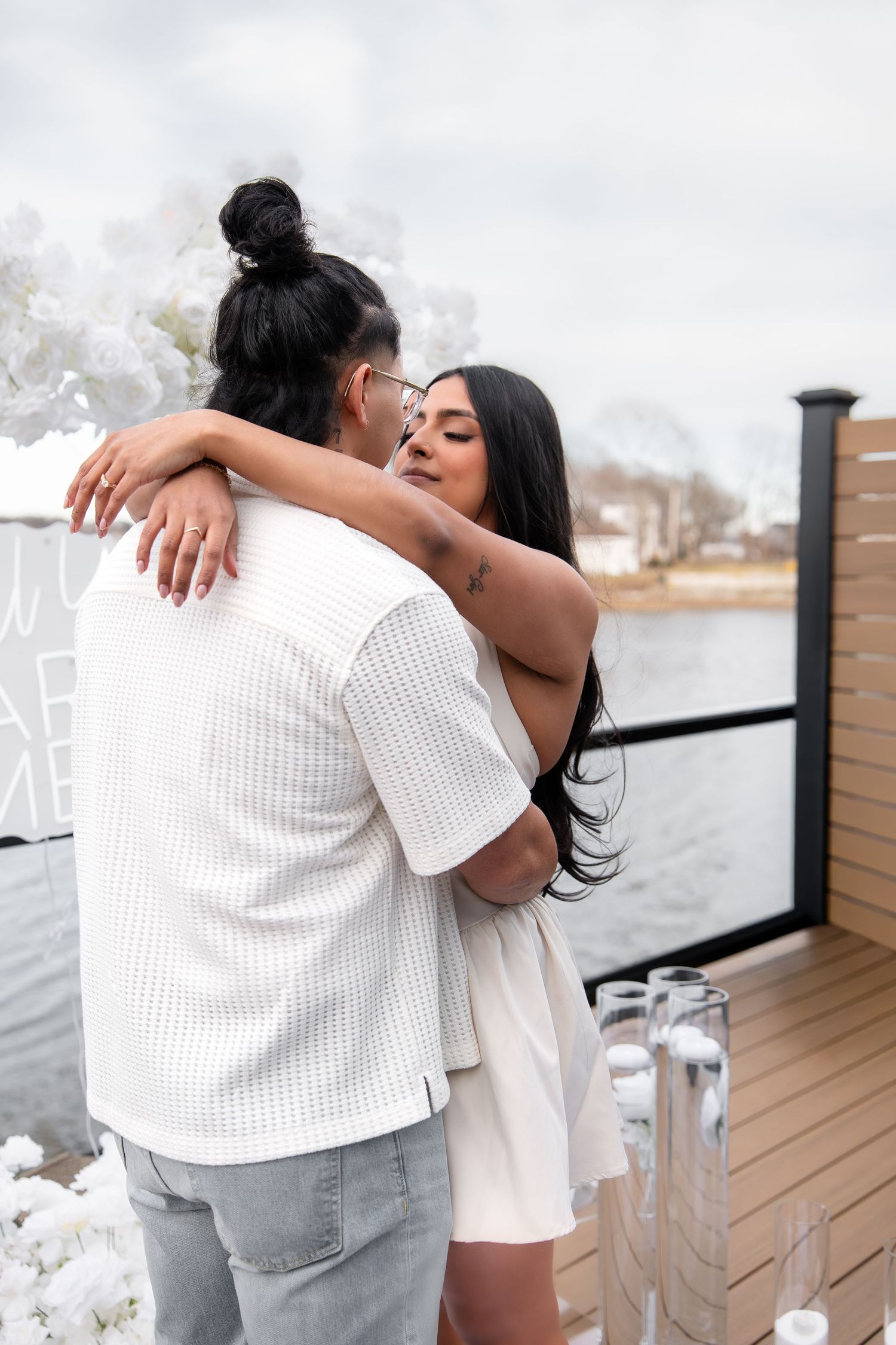 Couple embracing and kissing on a waterfront deck surrounded by white floral decorations.