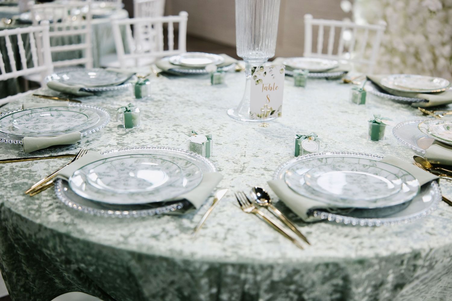 Elegant wedding reception table with sage green velvet linen, gold cutlery, and decorative charger plates.