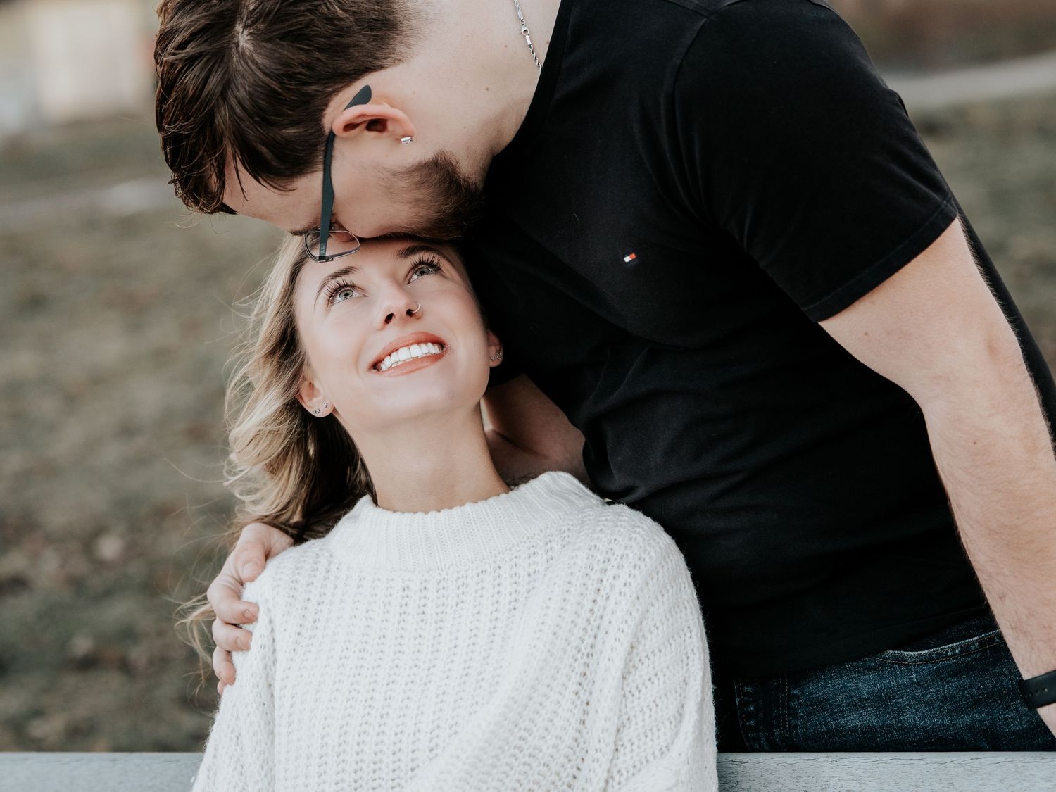 Man in black shirt kissing woman on forehead as she looks up smiling in a sweet outdoor couple portrait.