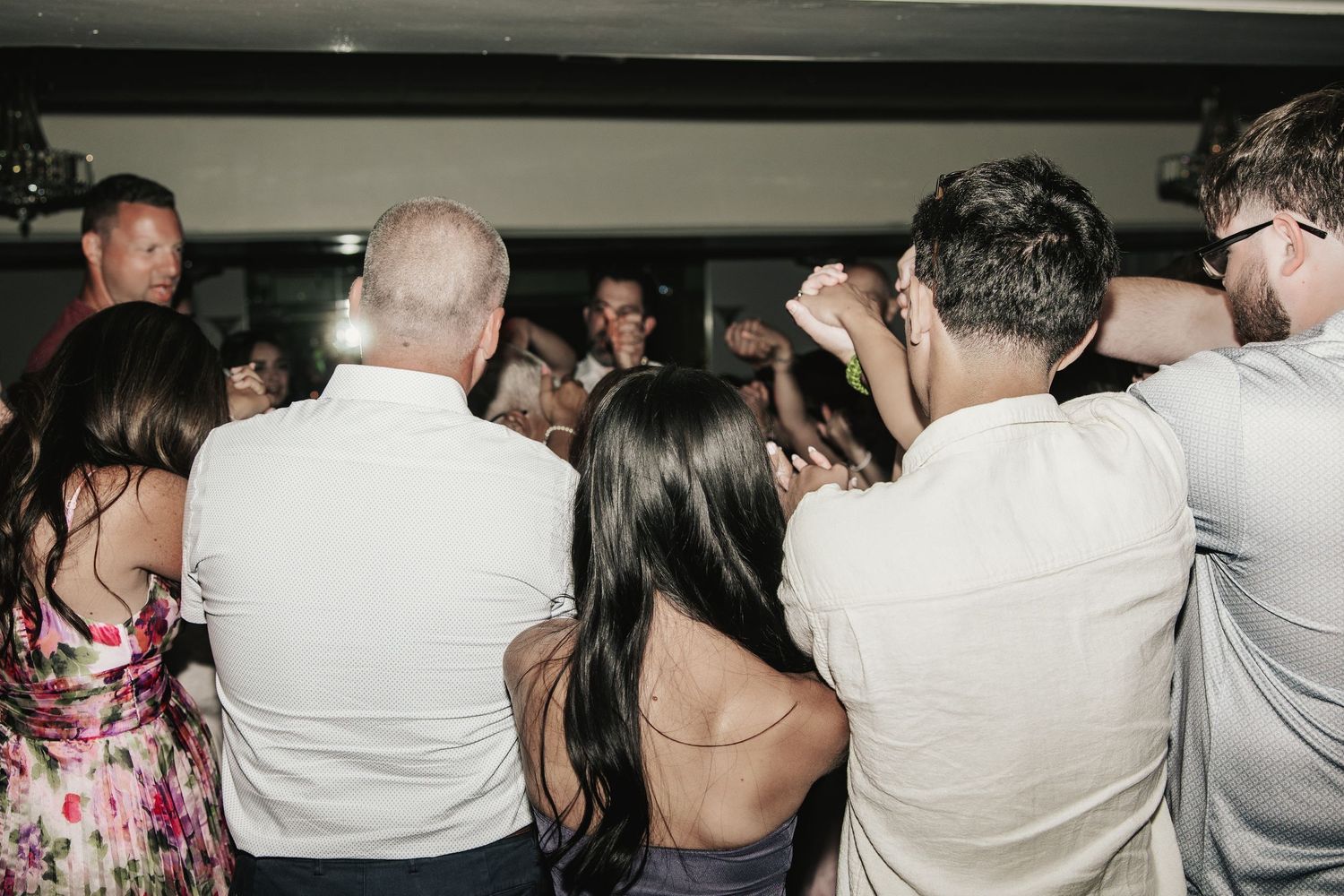 A lively crowd of people dancing closely together at an indoor party or wedding reception.