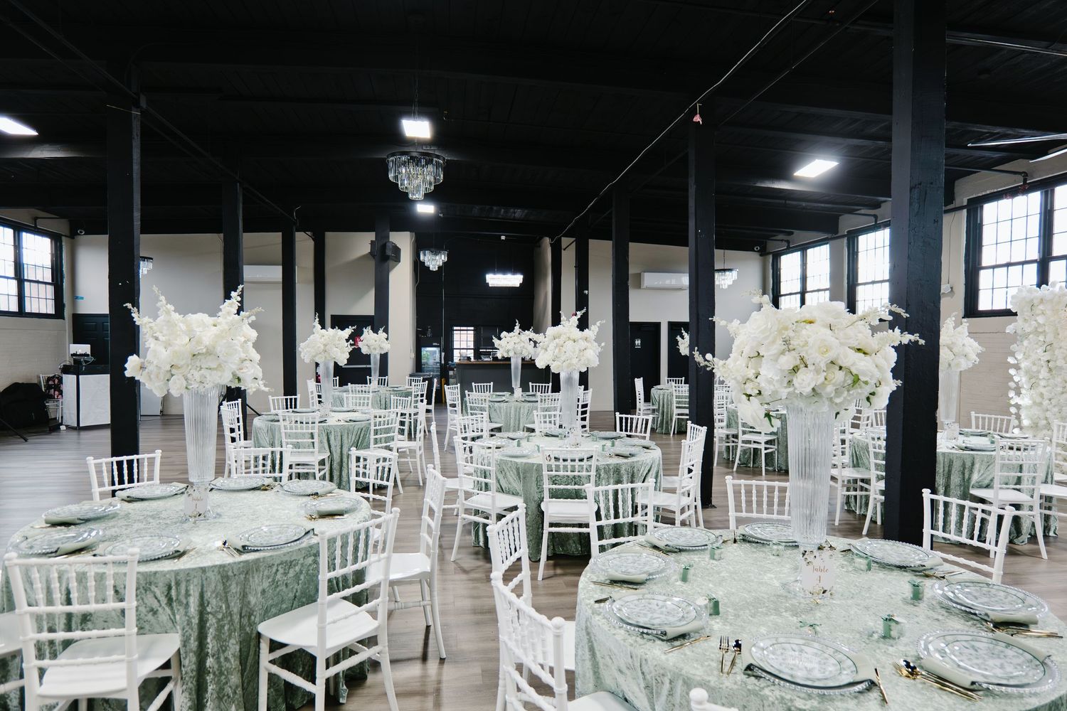 Elegant baptism reception hall with sage green tablecloths, white chiavari chairs, and tall floral centerpieces.
