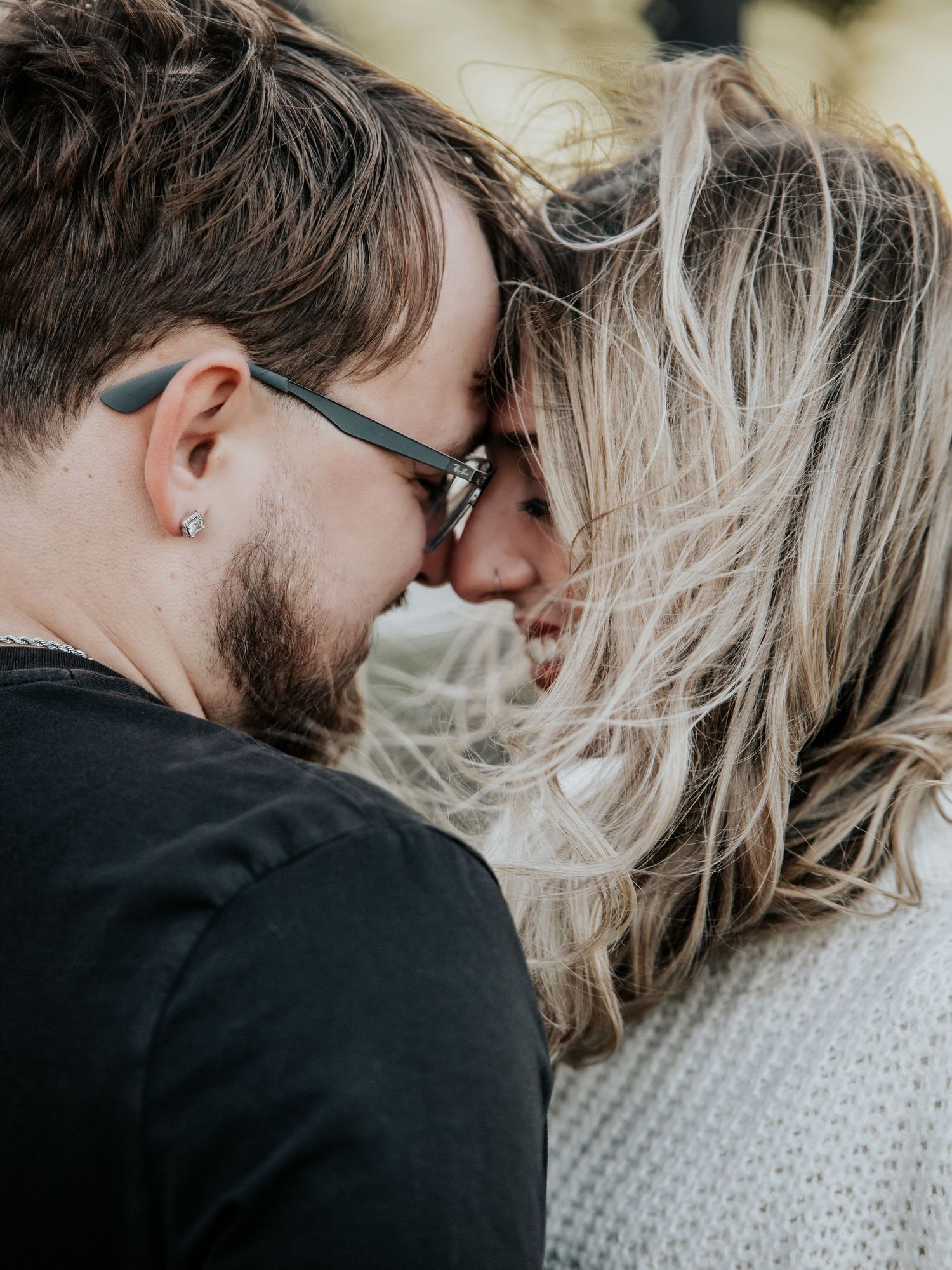 Close-up of couple with foreheads together, man wearing sunglasses and ear stud, woman with blonde hair.