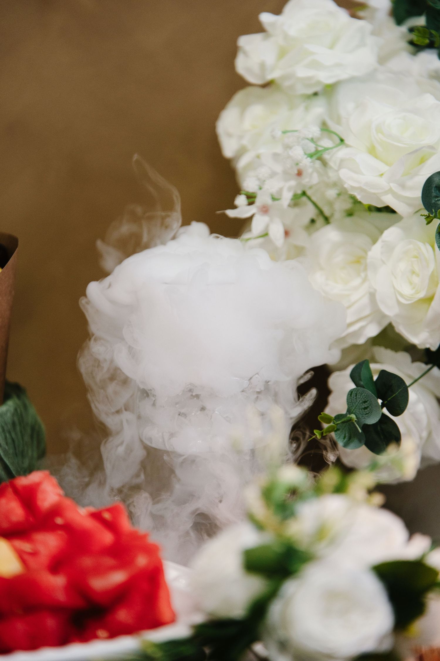 Dramatic dry ice effect billowing around fresh watermelon slices and white rose floral arrangement at a wedding reception.