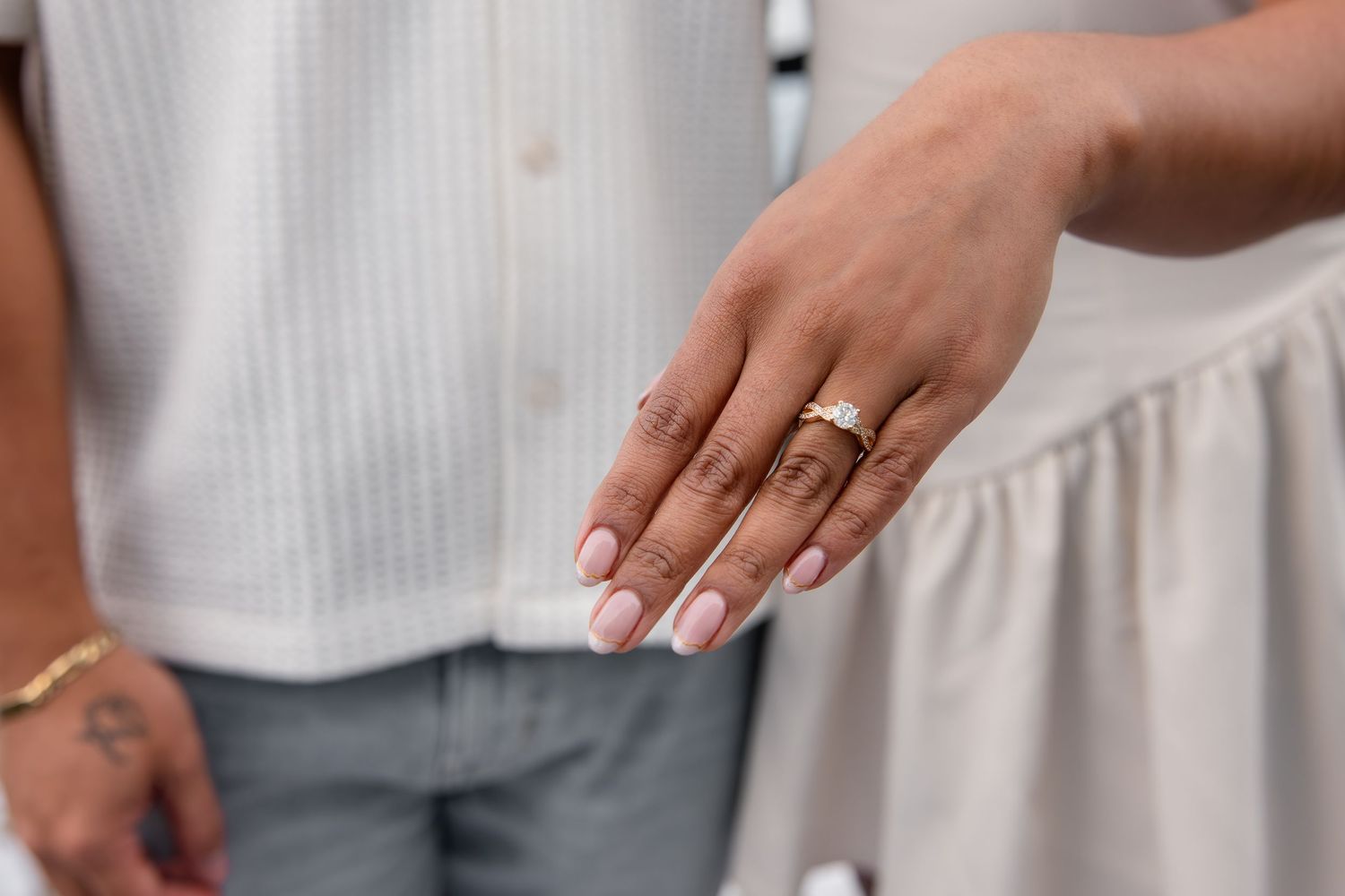 Close-up of a bride's hand showing a gold engagement ring with pink manicured nails at a wedding.