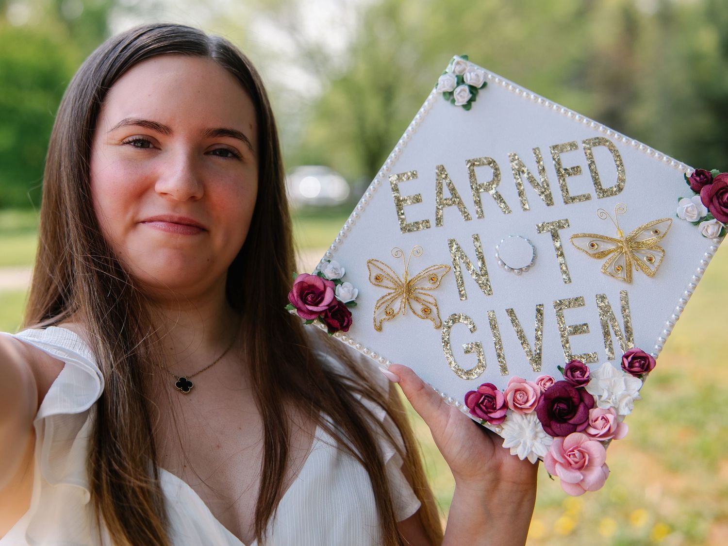 Nursing graduate proudly holding decorated cap reading Earned Not Given with floral accents and butterflies.