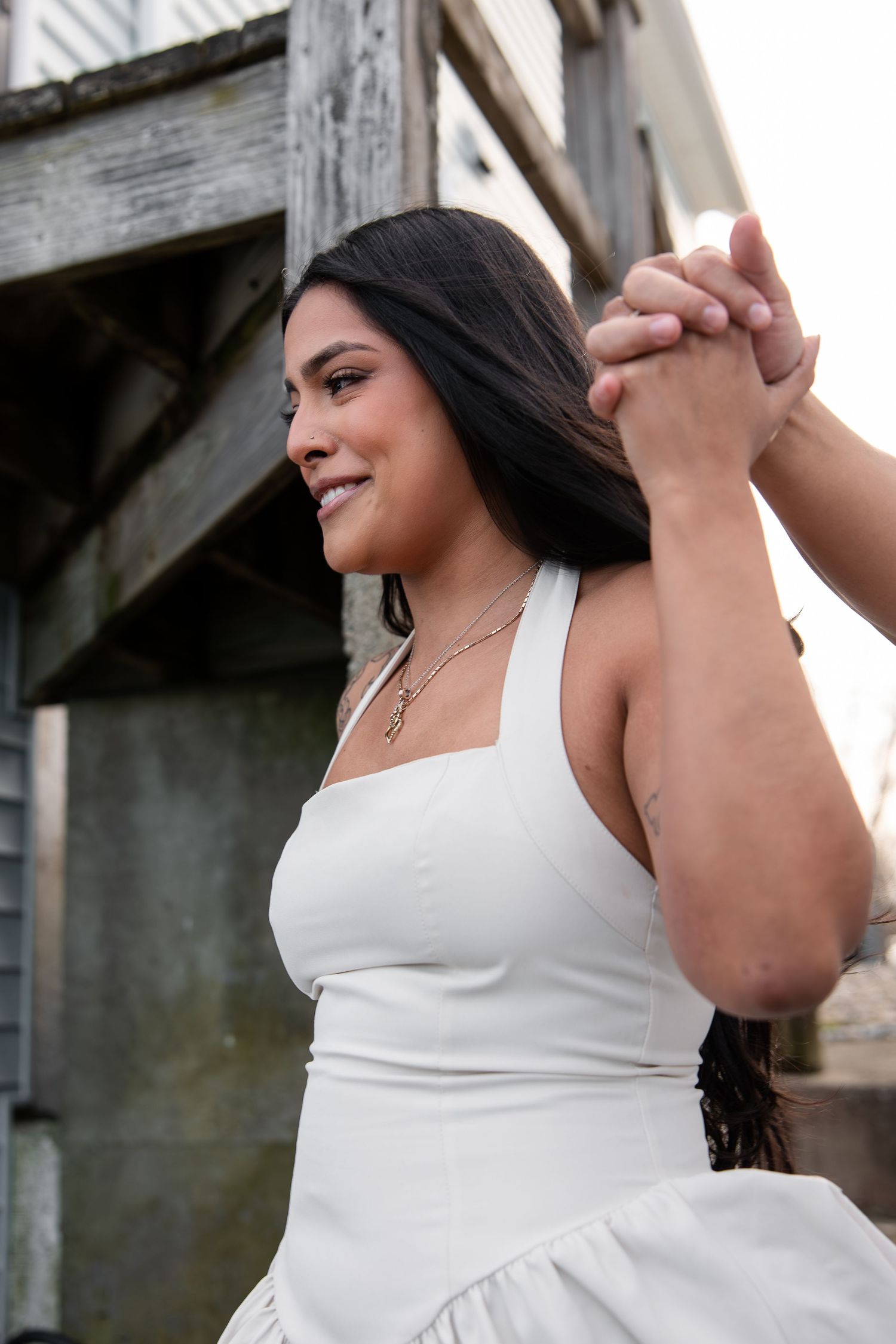 Woman in white dress smiling while holding hands during engagement photos.