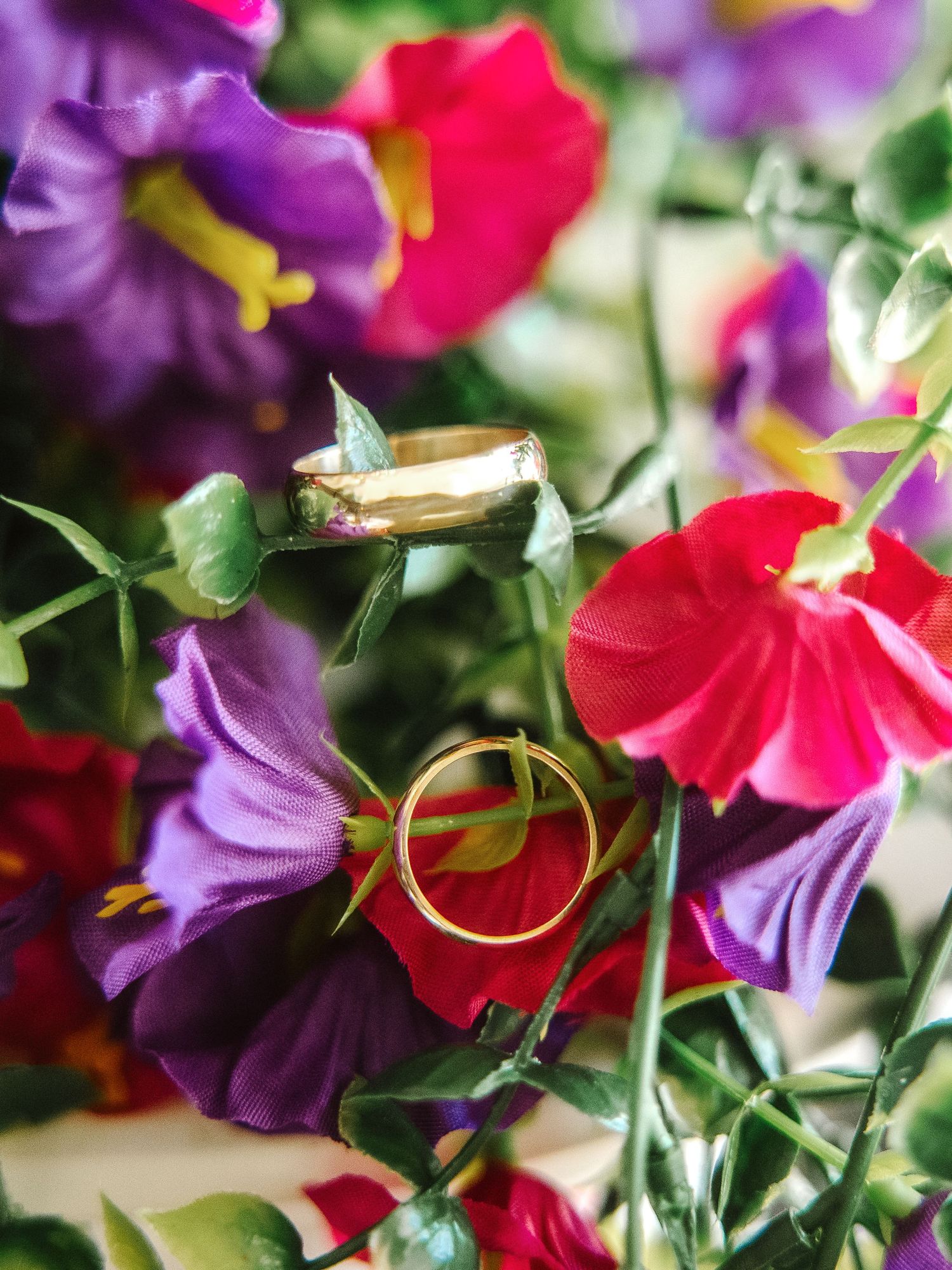 Two gold wedding rings nestled among vibrant pink and purple sweet pea flowers in a colorful bridal bouquet.
