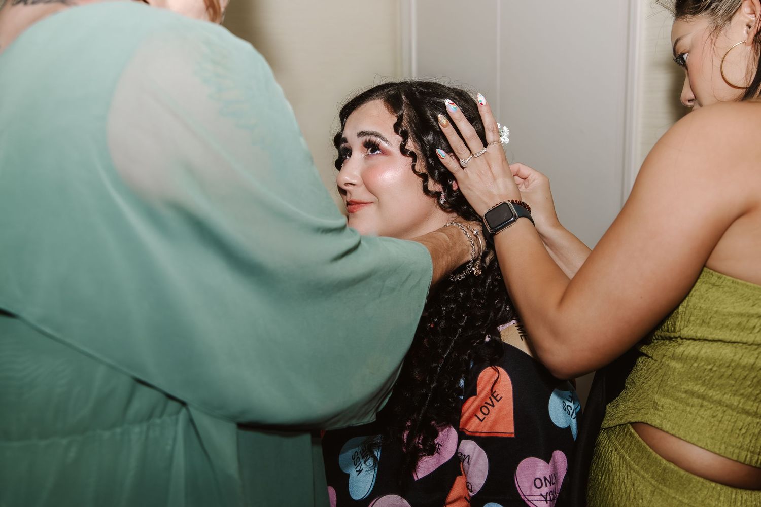 Two women styling a young woman's curly hair at a wedding celebration.
