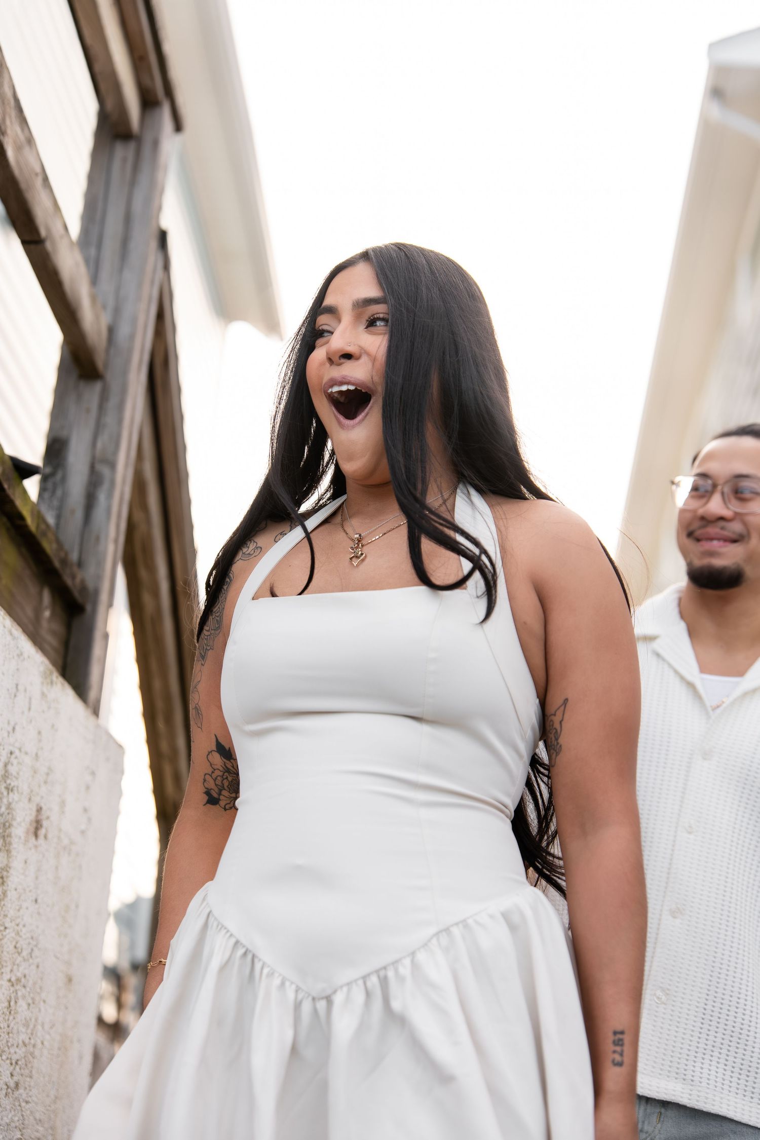 Woman in white dress laughing outdoors during engagement photoshoot.