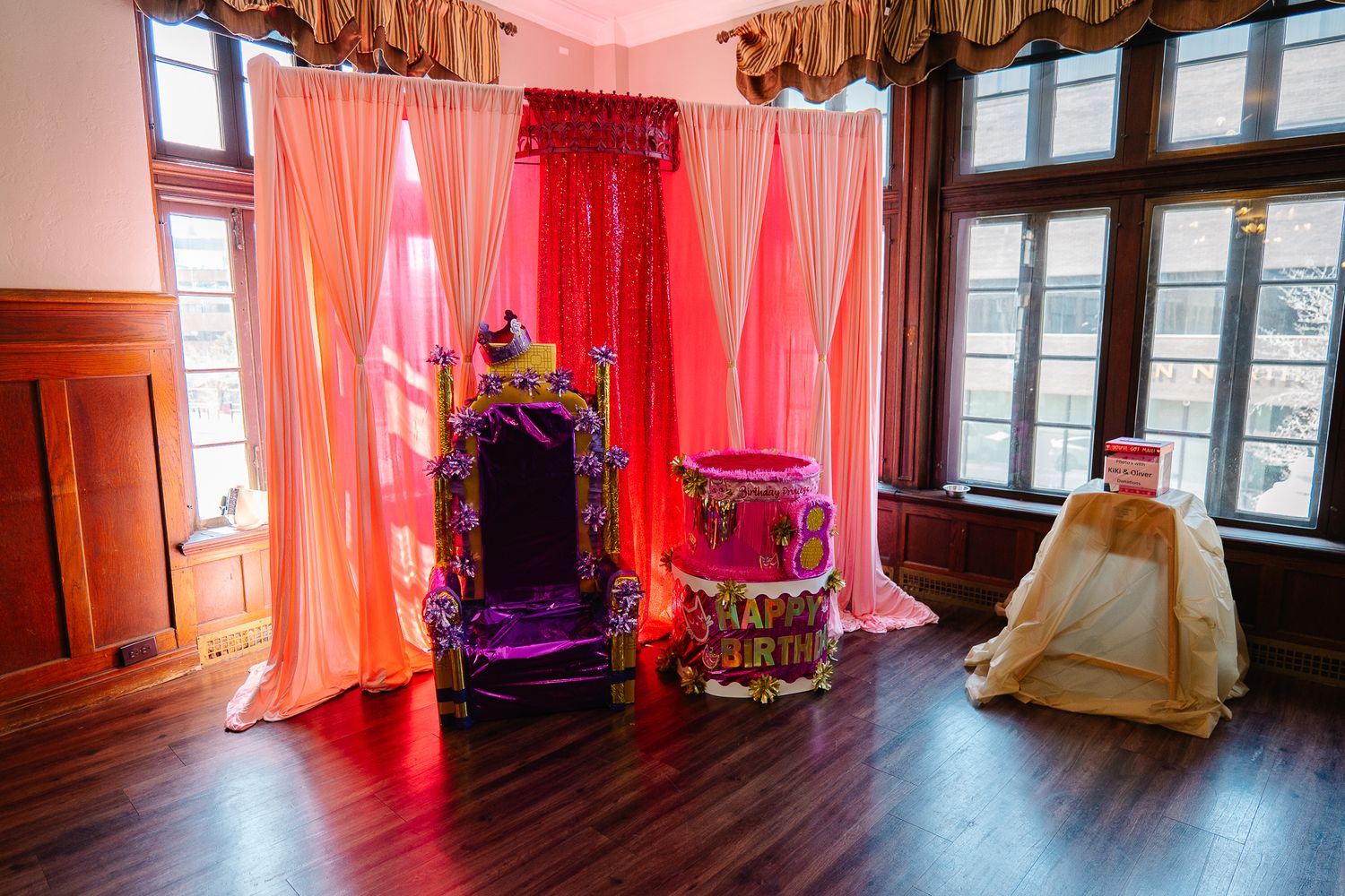 Vibrant pink and red draped backdrop with ornate throne chair setup for a royal birthday party event.