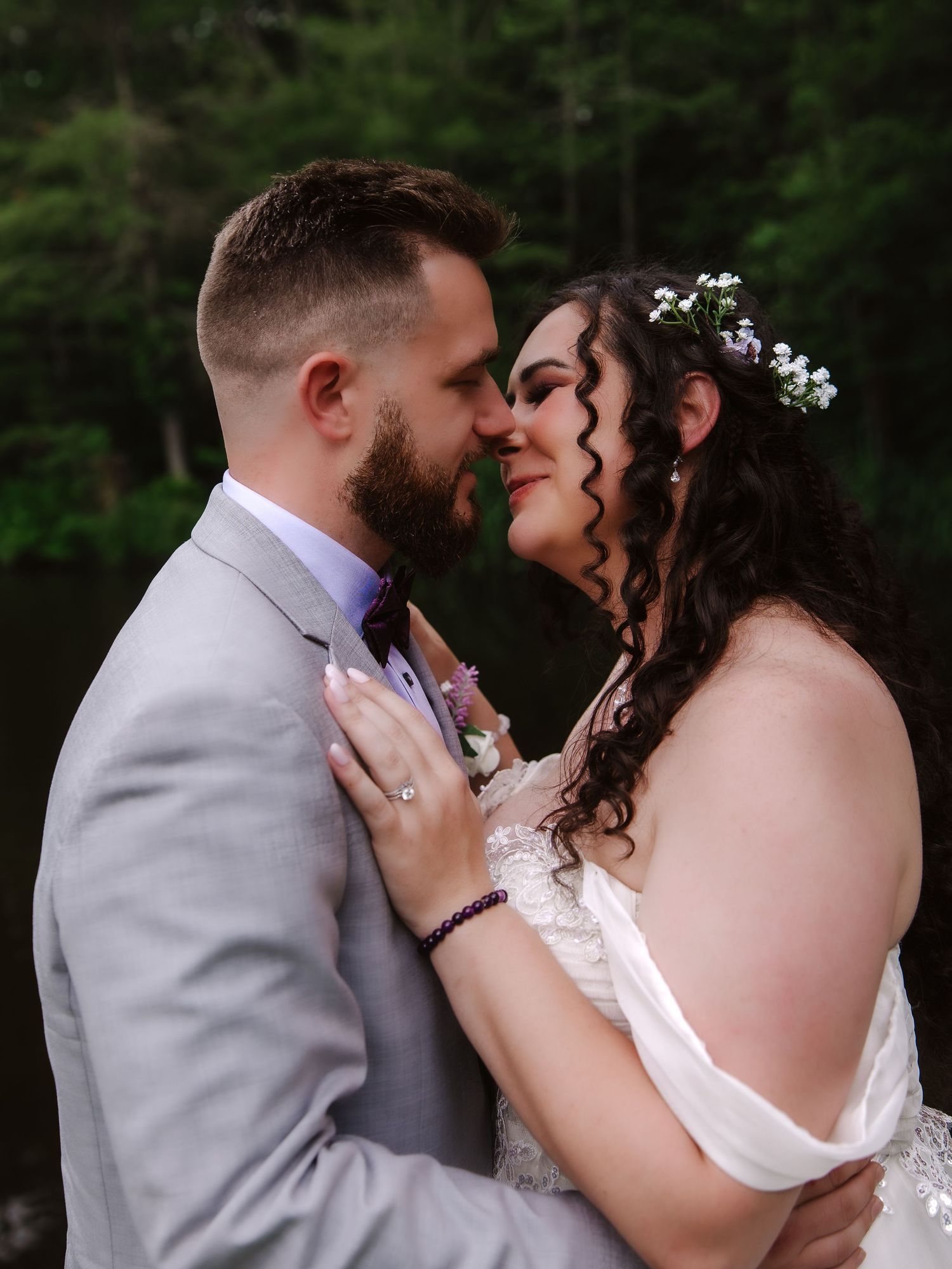 Bride and groom share intimate romantic moment, nearly kissing, bride wearing floral crown and lace gown.