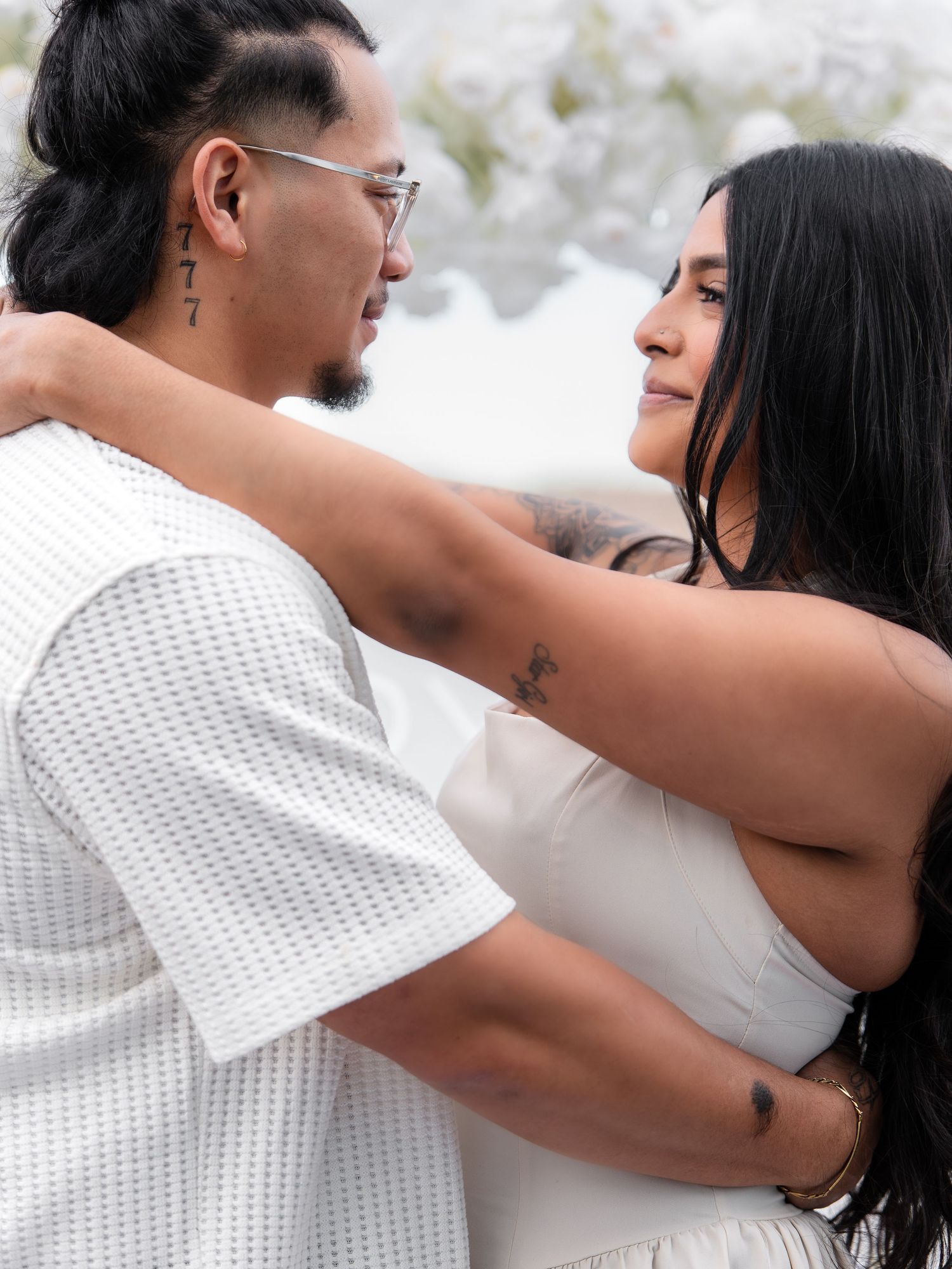 Couple in white outfits embracing and gazing at each other during a romantic proposal moment outdoors.
