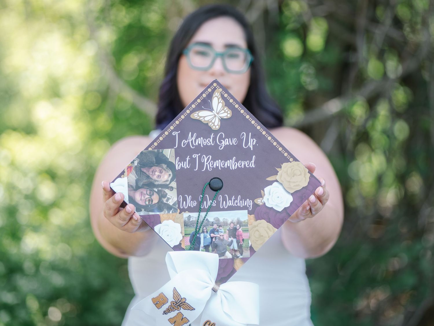 Graduate holding decorated mortarboard cap reading I Almost Gave Up But I Remembered outdoors.