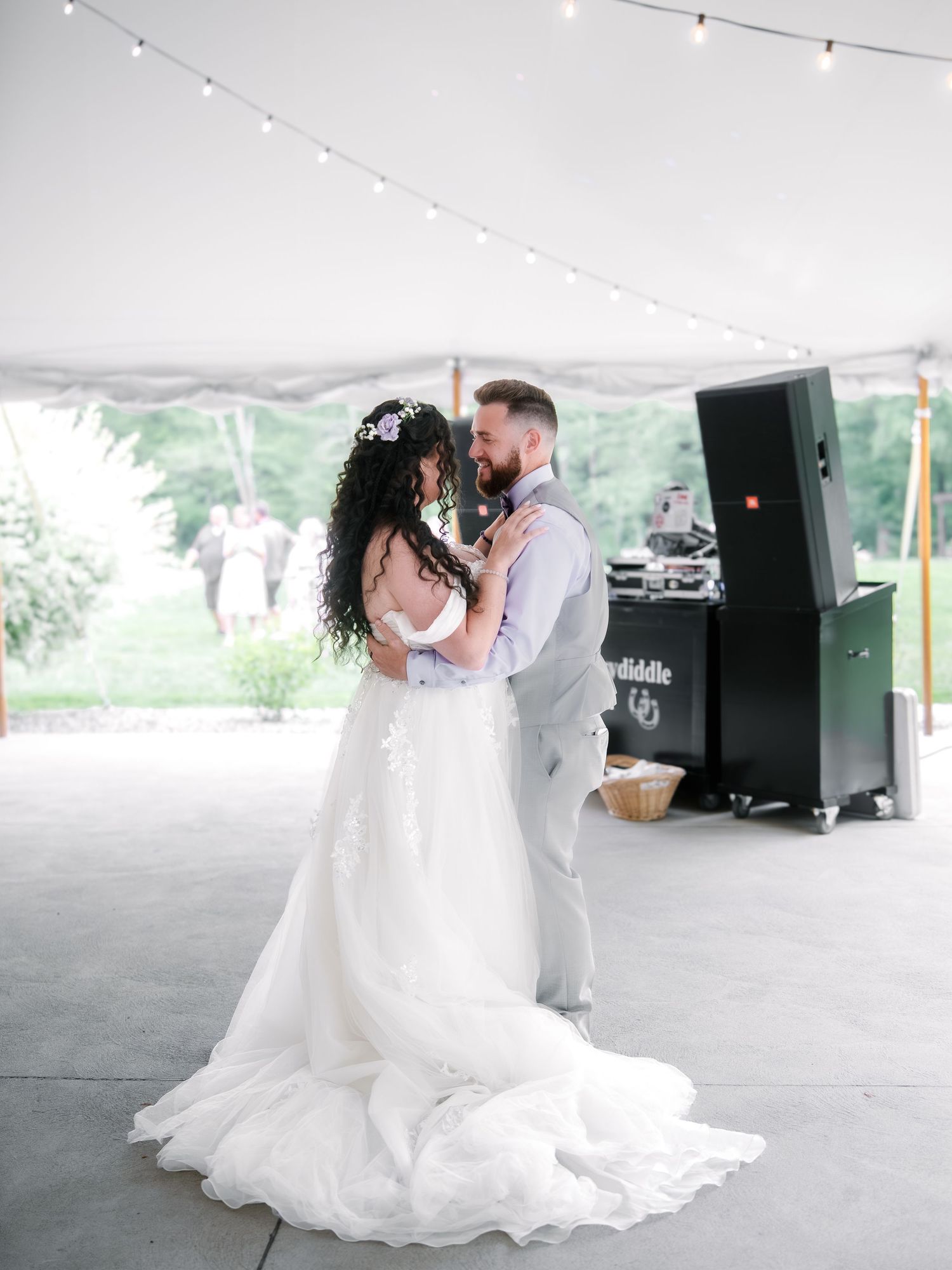 Bride and groom share first dance under a white tent with string lights at an outdoor wedding reception.